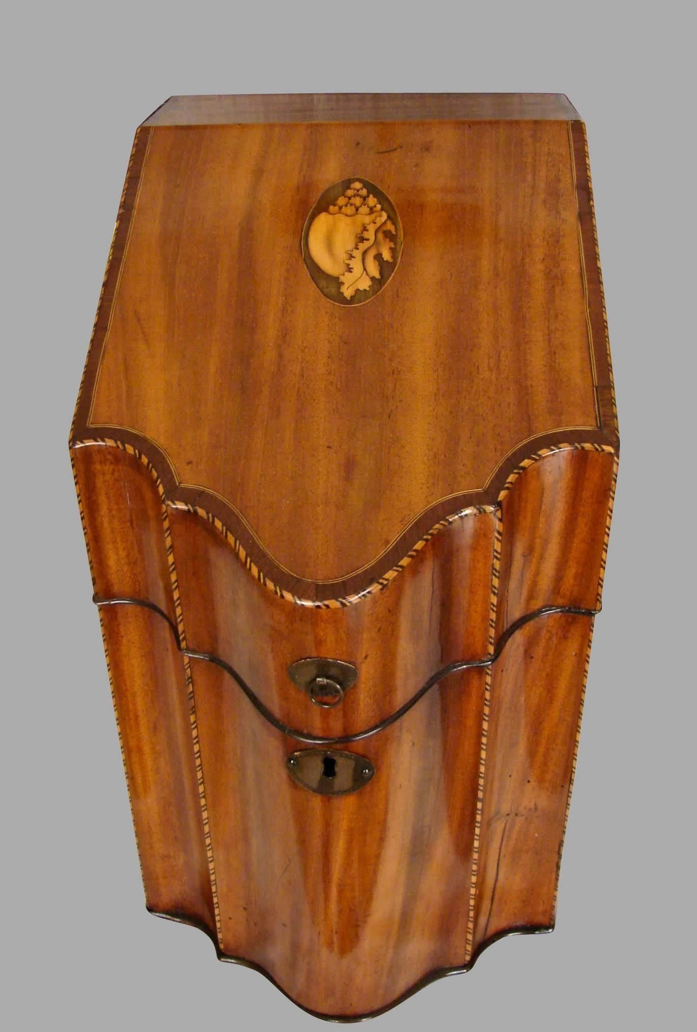 An English mahogany slant lid serpentine form cutlery box, the crossbanded top with inlaid boxwood conch shell decoration, an inlaid star on the underside of the lid, the interior retaining its original cutlery divides, the case with checkered