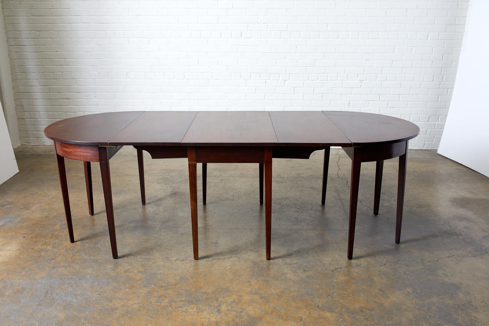 19th century English Hepplewhite style mahogany three part banquet or dining table. Set consists of one drop leaf table measuring 21 inches wide folded, and two demilunes. The table measures 52.5 inches with the leaves up and 93.5 inches wide with