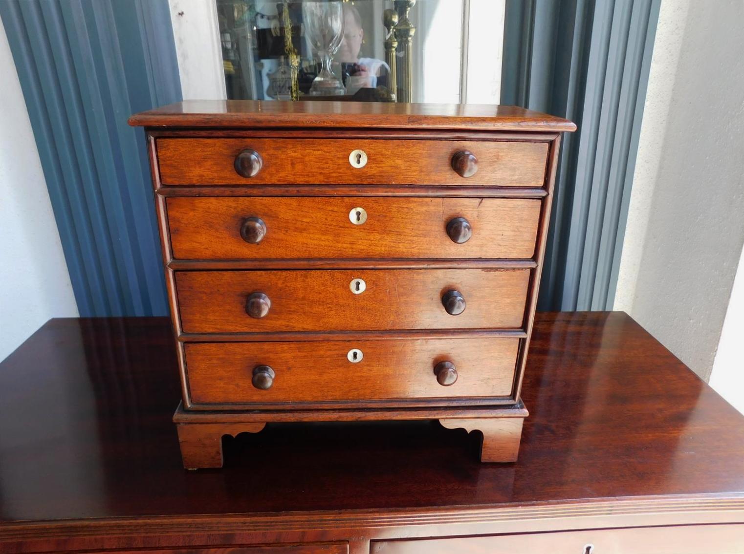 English Hepplewhite Mahogany miniature chest of drawers with a carved molded edge top, four graduated drawers, original wooden knobs with mother-of-pearl inlaid escutcheons, and resting on the original bracket feet, Late 18th Century Secondary wood