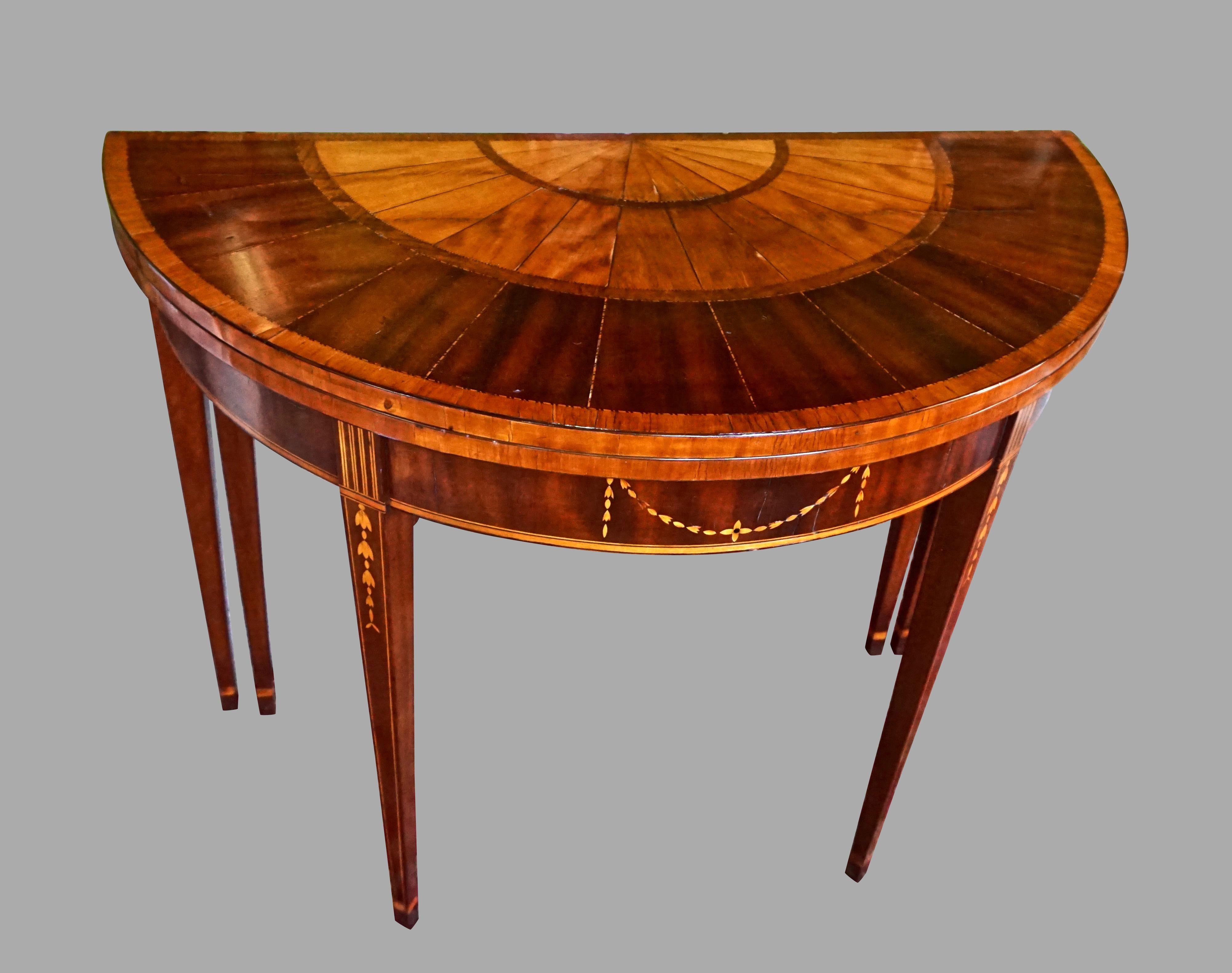 A very pretty English mahogany satinwood inlaid flip-top games table, the demilune top inlaid with concentric bands of satinwood and mahogany separated with boxwood divides, the apron with a central swag inlay, supported on square tapered front legs