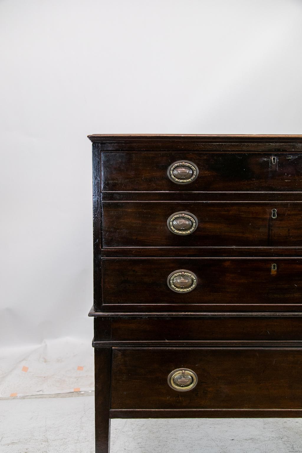 The top of this English Hepplewhite secretaire has two drawer fronts that drop down to reveal the secretary interior. There are six small and two larger drawers which have the original brass knobs. There is a small drawer inside the prospect door.