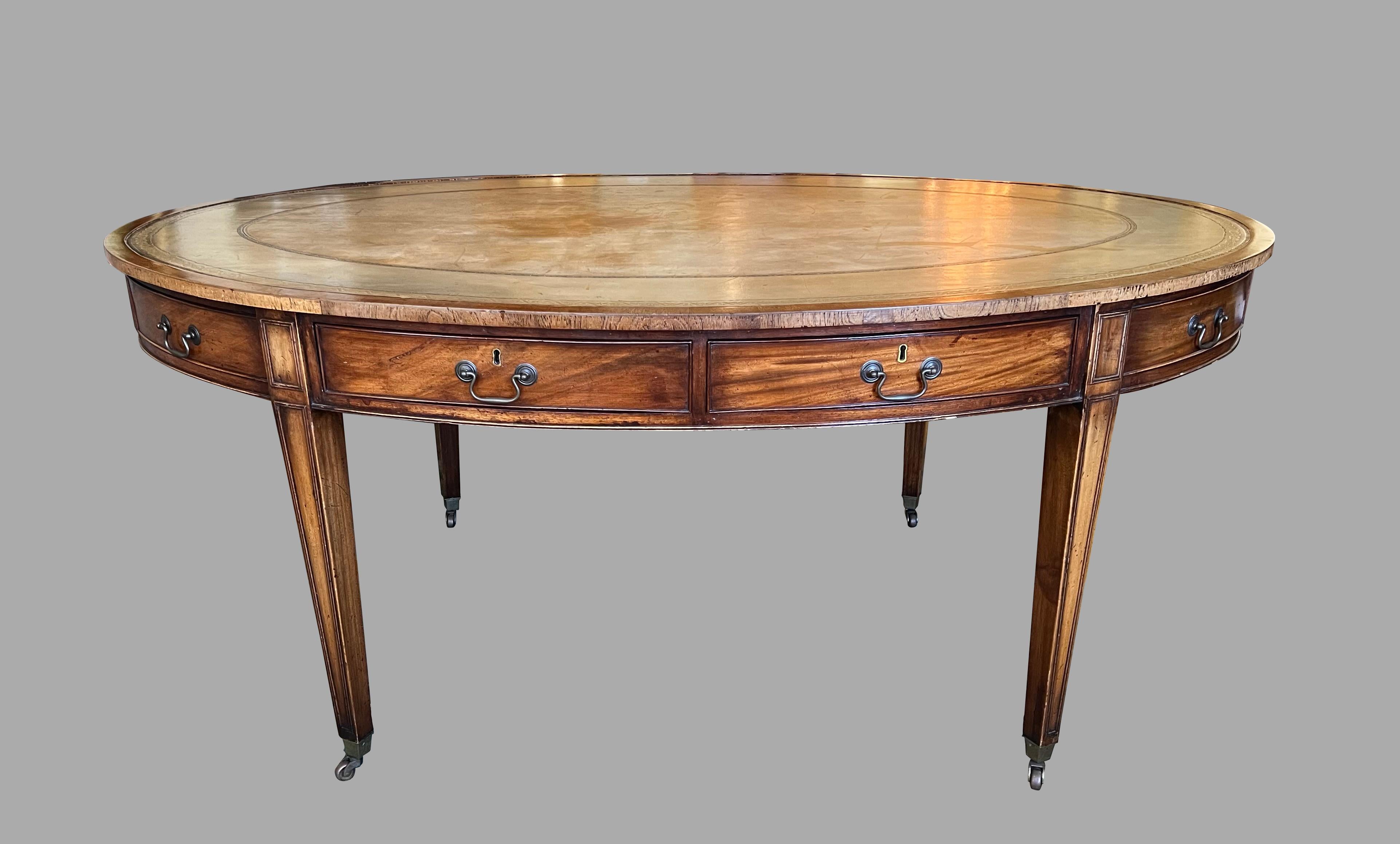 An unusual English oval writing table of large size, the gilt-tooled faded brown leather top above 4 functional and 4 false cockbeaded drawers with brass keyhole escutcheons and bail handles. The piece is supported on molded square tapered legs