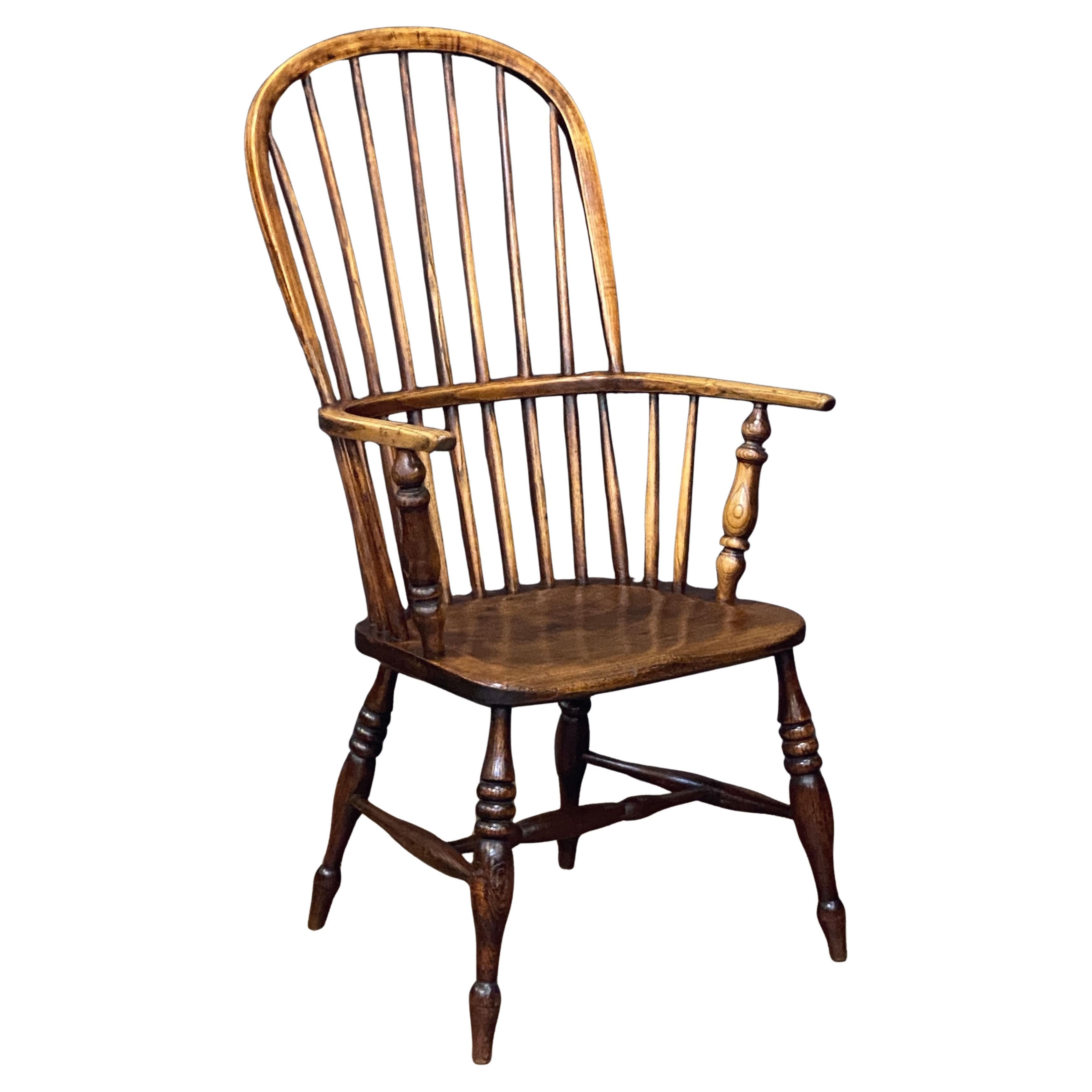 A handsome Windsor high back armchair of elm from Georgian era England, featuring a bowed top rail and spindle back, with curved rail arms mounted to a shaped solid seat, and set upon a turned stretcher base.