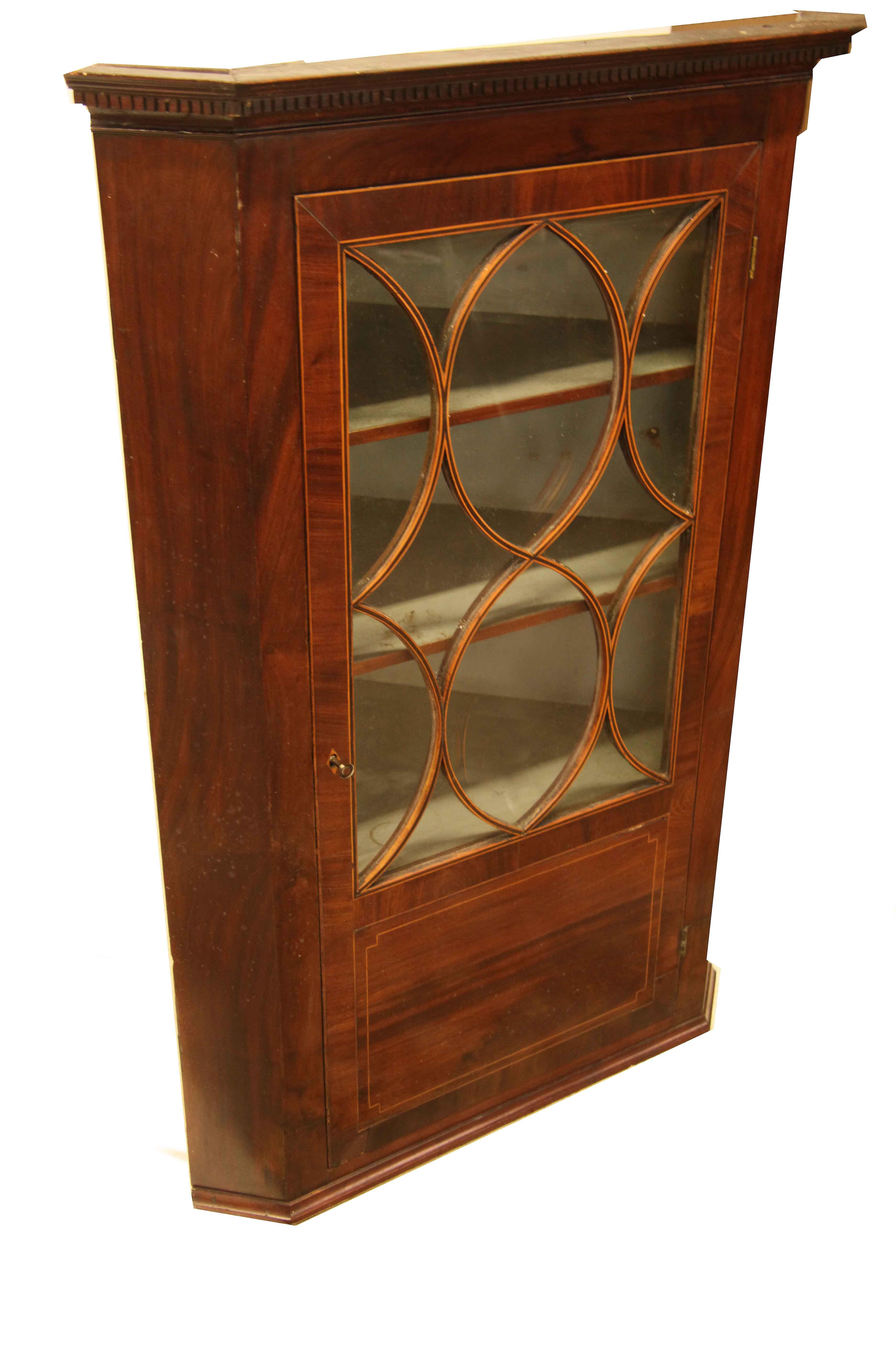 English inlaid glass door hanging corner cupboard, the cove cornice features bold dentil molding, the glass door is cross banded with mahogany and has curvilinear muntins faced with bands of mahogany and boxwood; lower portion of the door has a
