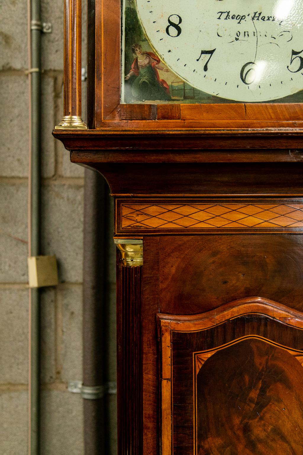 Cette horloge est abondamment incrustée de bois de rose, d'ébène, de satin et de buis. Le bonnet comporte deux pateries en coquillages incrustés. La porte centrale présente une incrustation d'urne classique (fleur et feuille) ainsi que le panneau