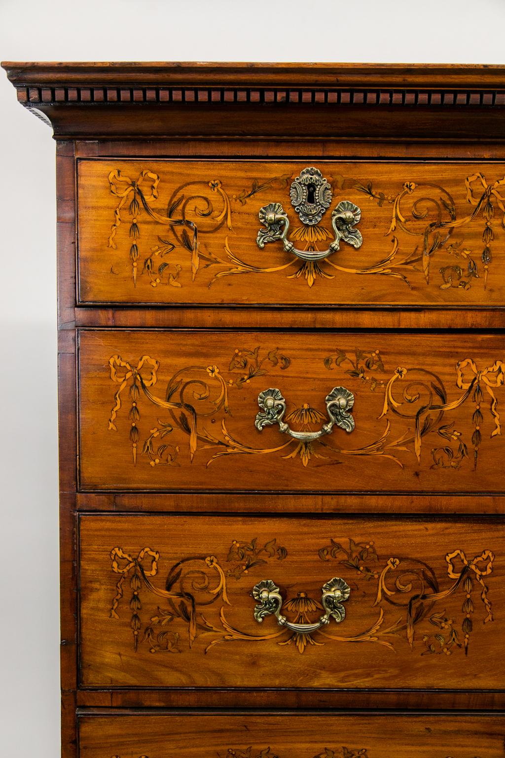 The drawers of this chest on frame have incised cockbeading and are inlaid with satinwood, ribbons, bellflowers, and arabesques. The base has inlaid fans in a scrolled apron. The legs are turned with stylized ionic capitals and terminate in a