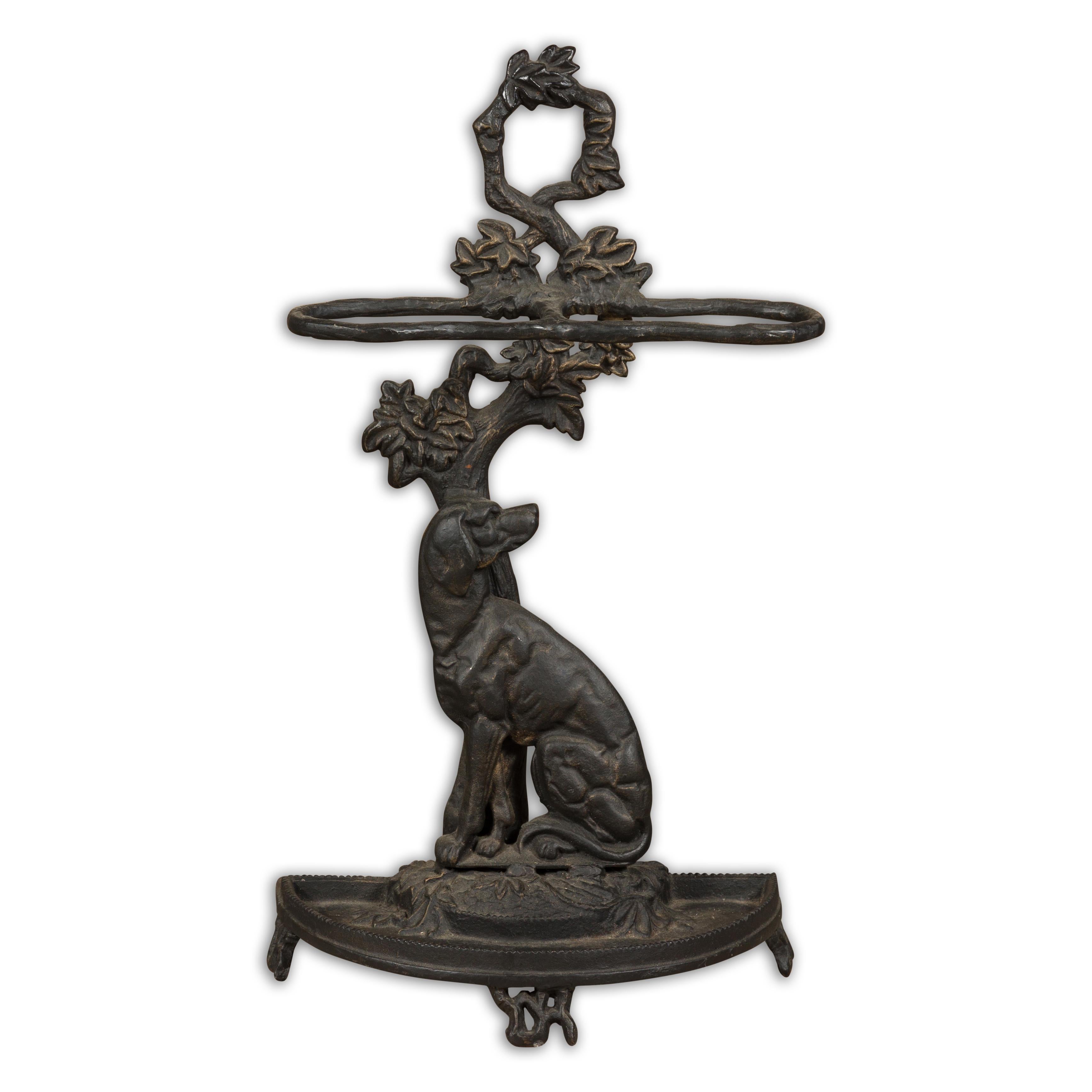An English iron umbrella stand from the 20th century depicting a dog obediently sitting in front of a tree. Embrace the whimsical charm of this 20th-century English iron umbrella stand, a perfect amalgamation of practicality and aesthetic appeal. A