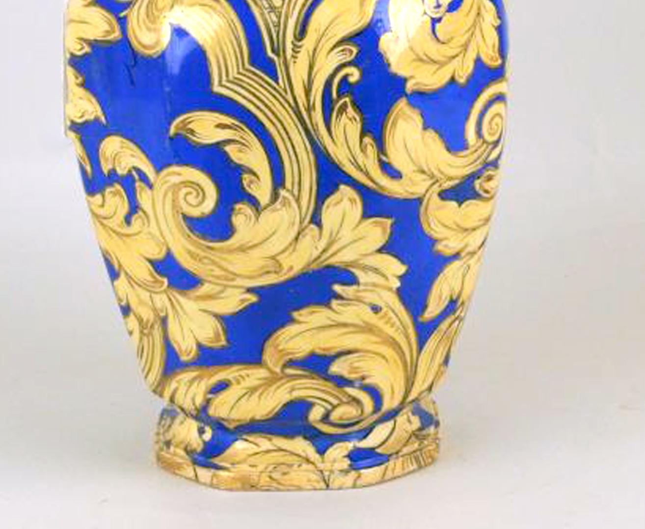 The octagonal-from vase has a deep blue ground and is painted in gilt and yellow with Rococo scrolls of foliage and vases of flowers. The dragon scroll handles and decorated with gilt heighten yellow, The double dolphin finial is similarly