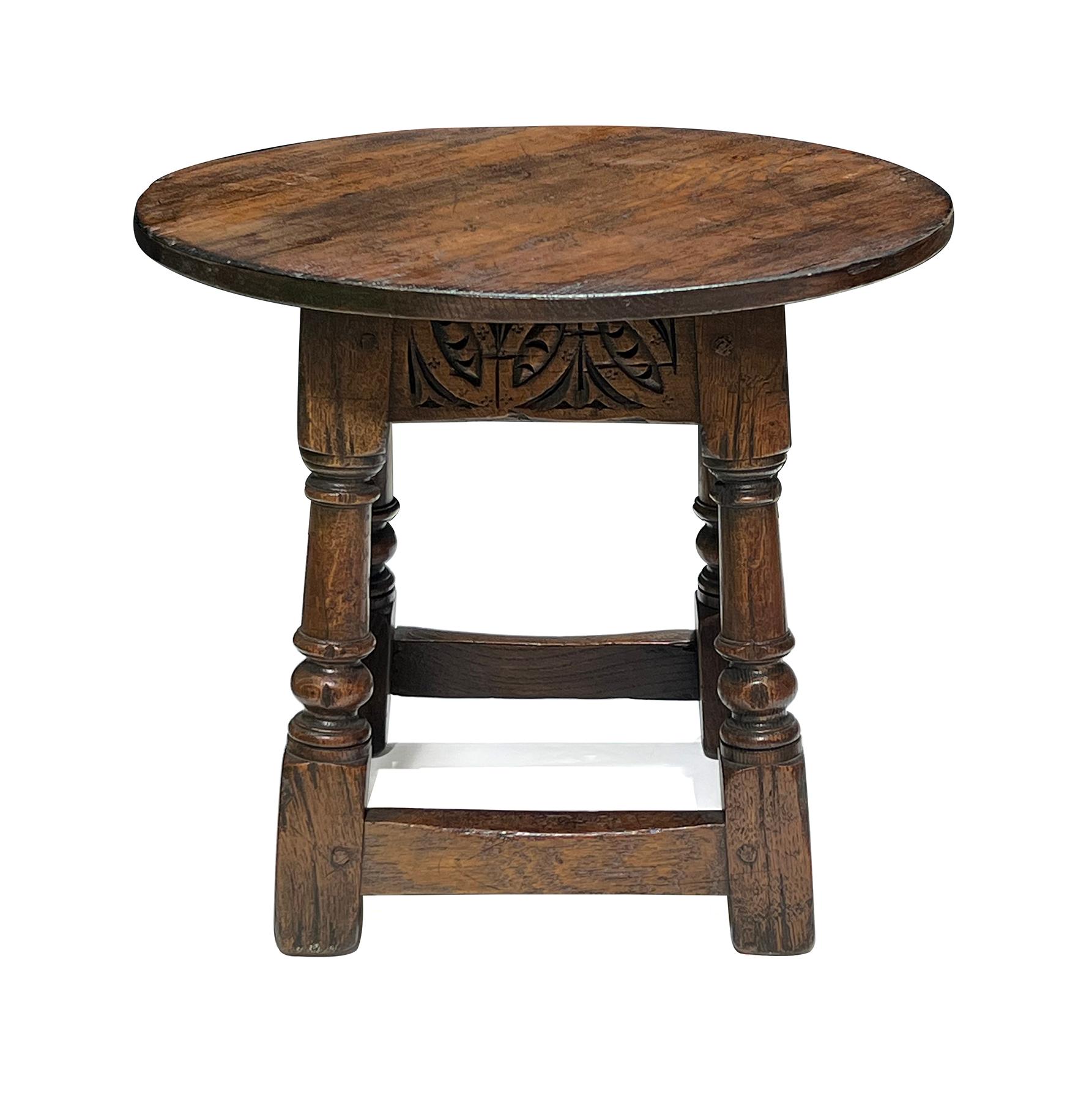 the solid oak circular top above a carved apron adorned with Jacobean motifs all raised on four turned supports ending in block feet all joined by perimeter stretchers; structurally sturdy with pegged construction