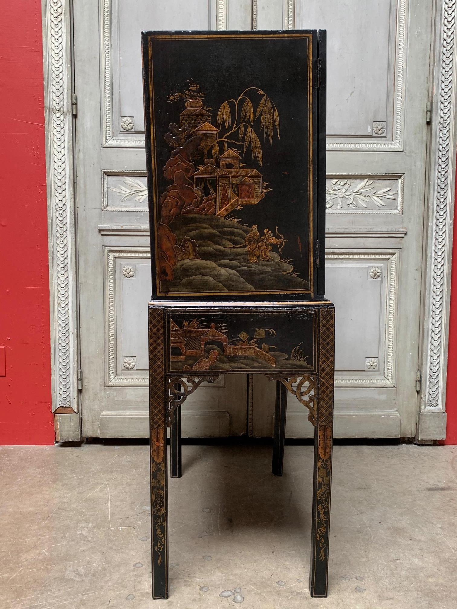 English chest on stand with a Japanned lacquered finish in black, gold and red dating from the mid-19th century. This cabinet has two doors with Chinoiserie decoration both on the exterior and interior, open to a concealed interior of decorated