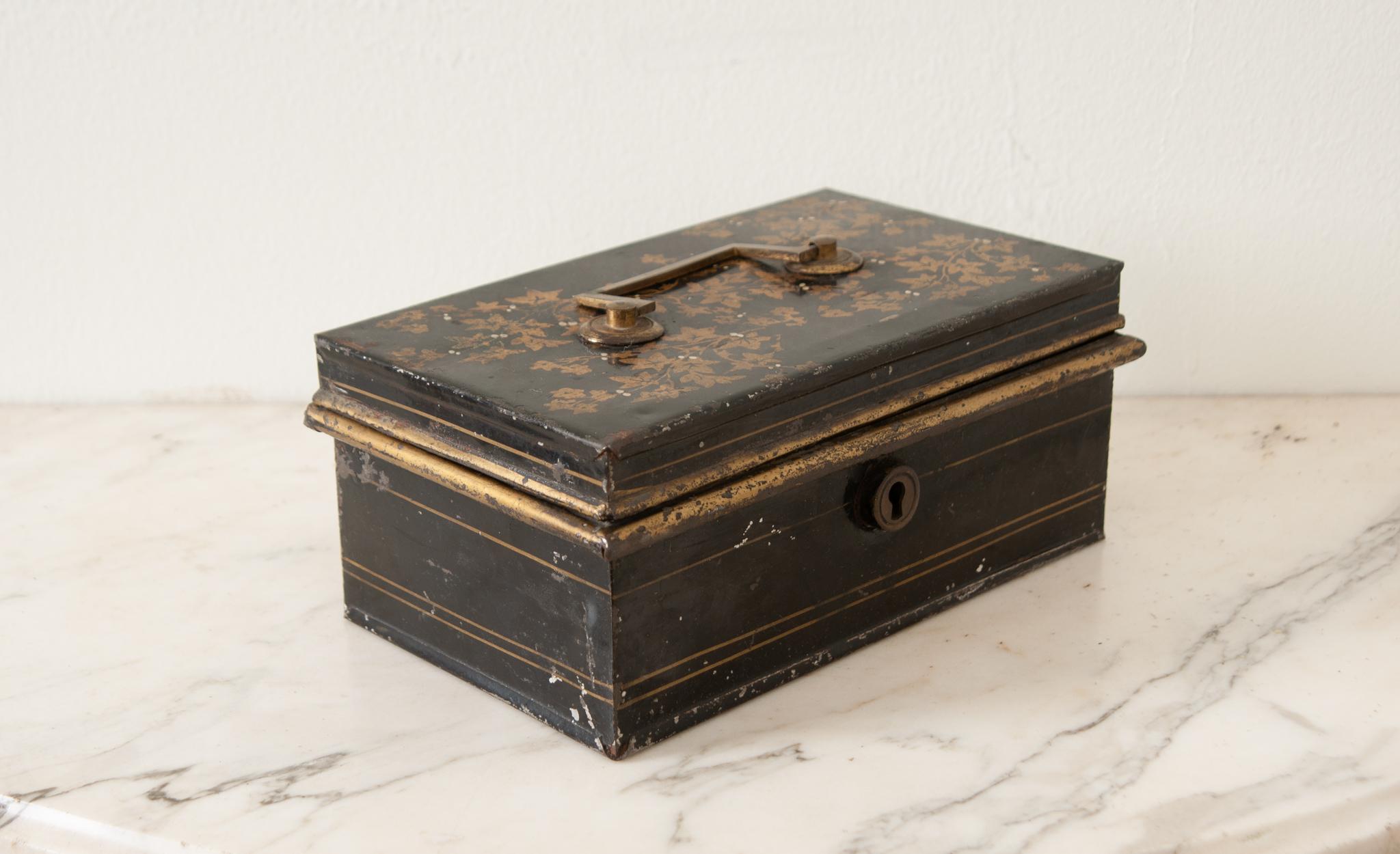 An English black tole box from ‘John Moreton & Company, Wolverhampton”. This small box has gold painted ivy designs with a brass center handle and opens to a fitted interior with two levels of storage. The top level has two compartments with hinged