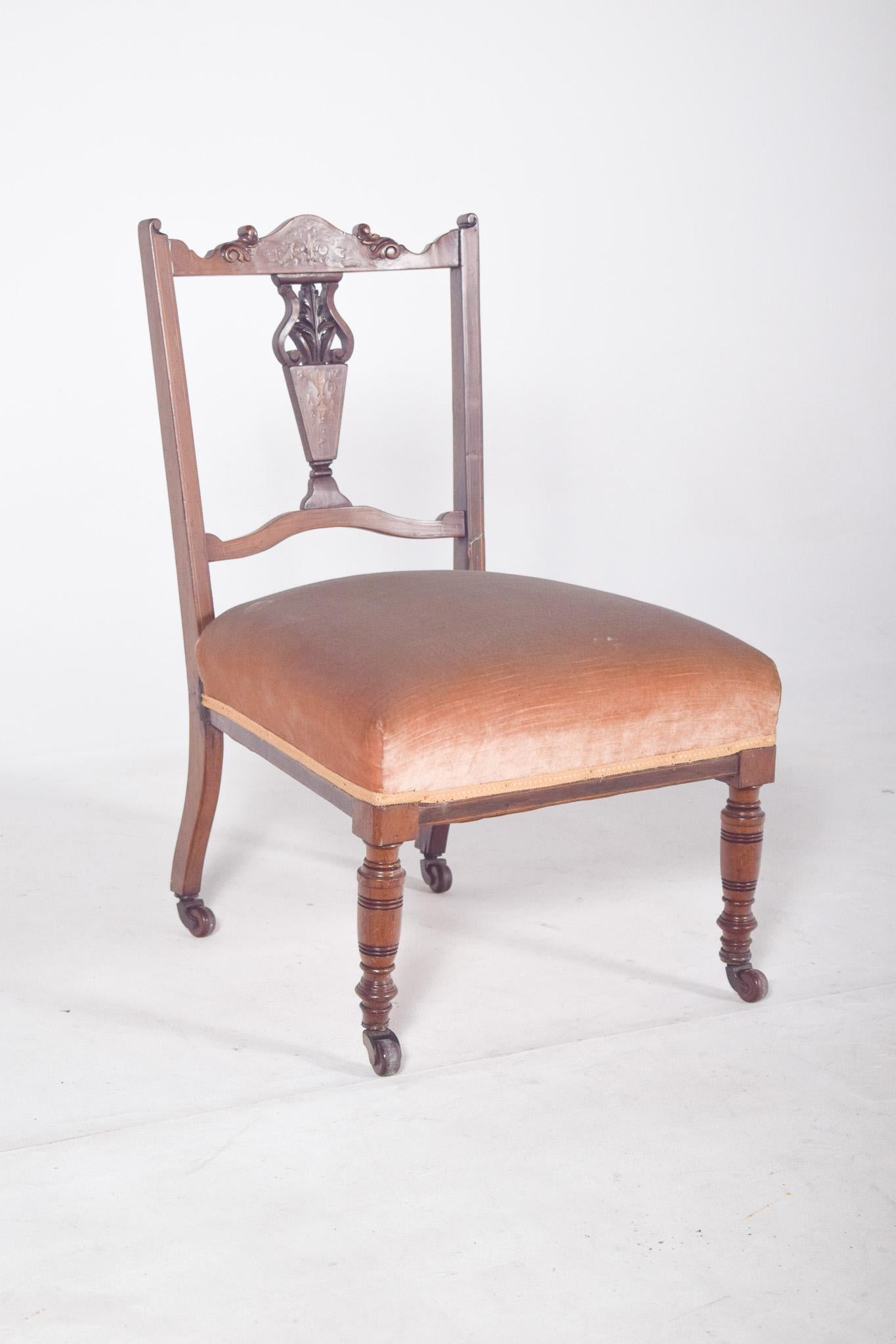 Fauteuil de dame en bois de rose. Le dossier est décoré de sculptures et de marqueteries, avec un élément central ajouré en forme de vase avec des feuilles, flanqué de courbes symétriques. La partie supérieure du dossier est ornée d'une frise