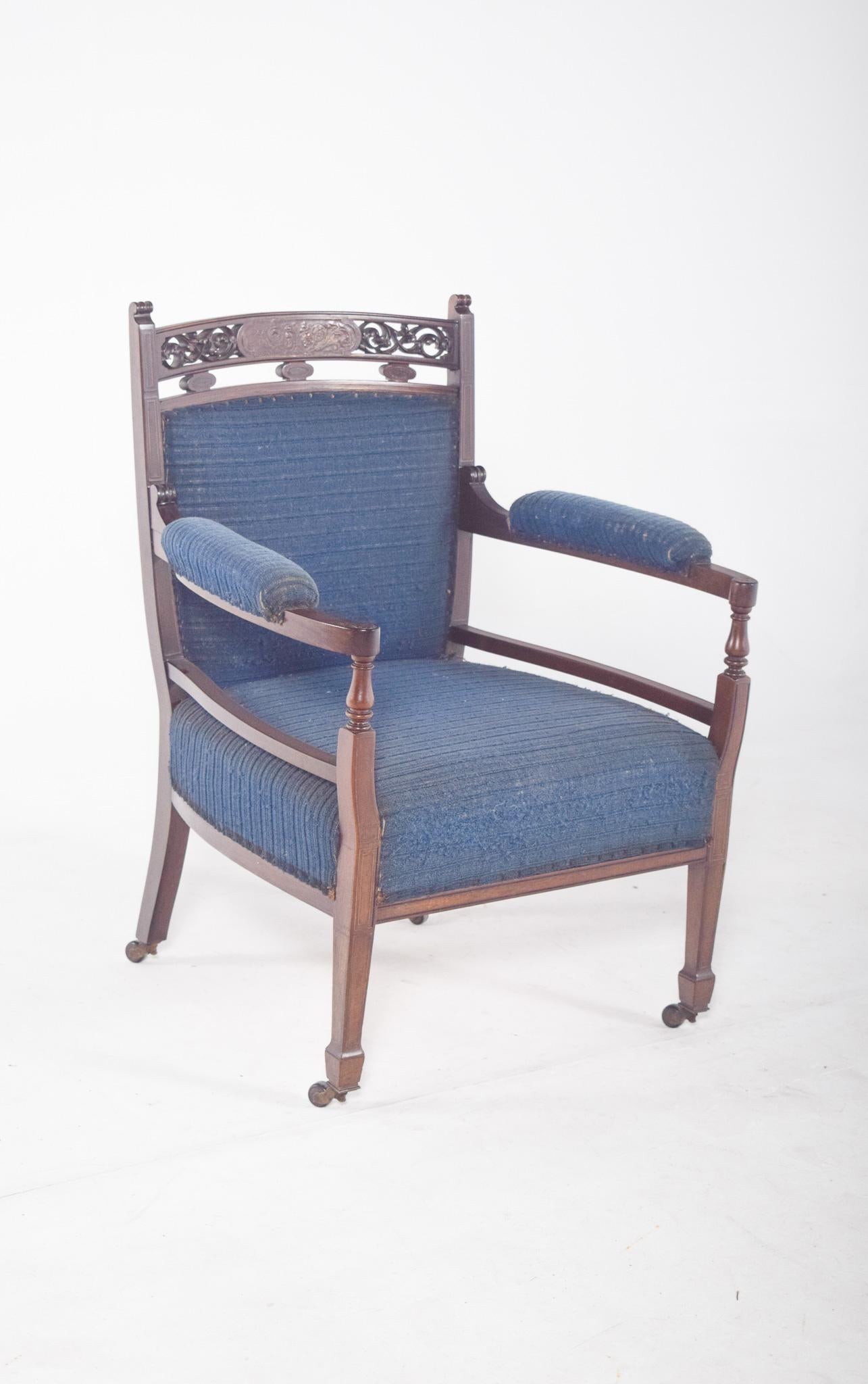 Petite chaise, tapissée en bleu. Dossier haut, finition en dentelle de bois sculpté avec des motifs végétaux et une forme ovale. L'assise, le dossier et les accoudoirs sont revêtus d'un tissu bleu avec un discret motif de rayures horizontales. La