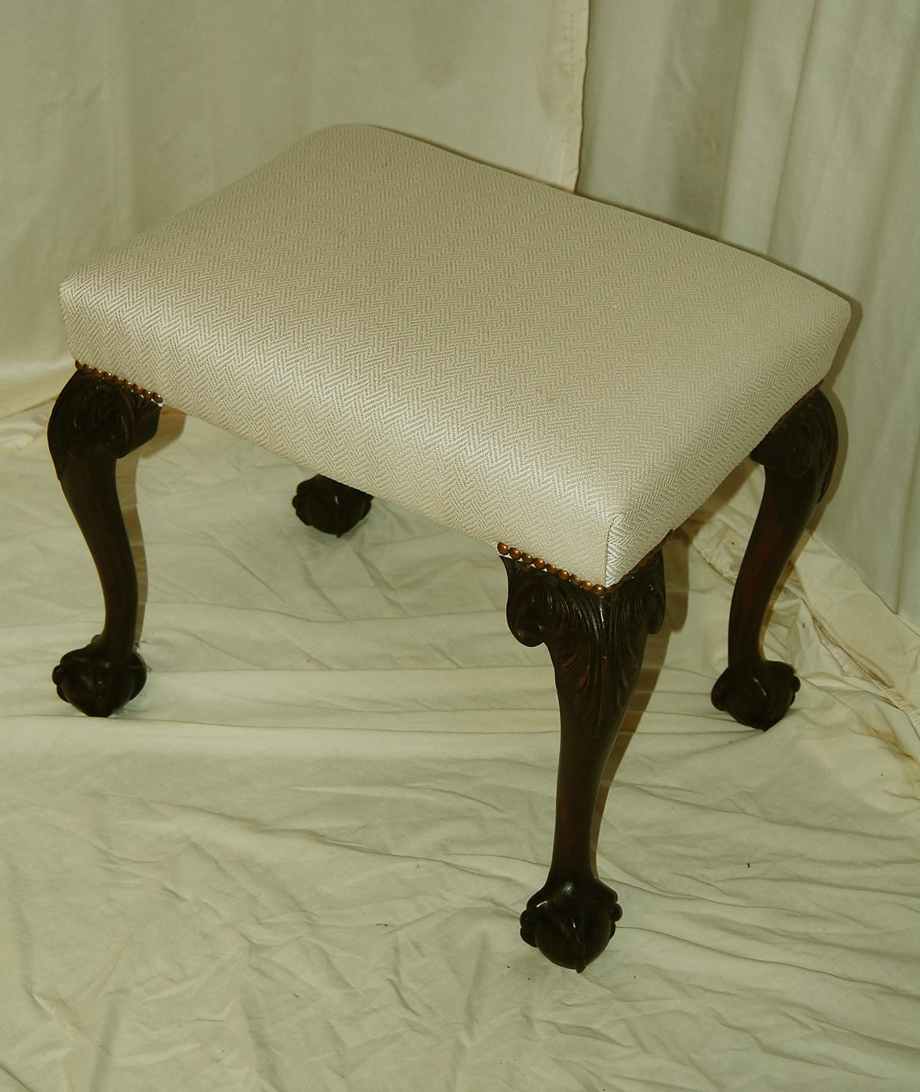 English Chippendale style mahogany stool with cabriole legs. The cabriole legs are hand carved with acanthus leaves on the knees and end in ball and claw carved feet. This classic stool is well executed and has been upholstered in a cream colored