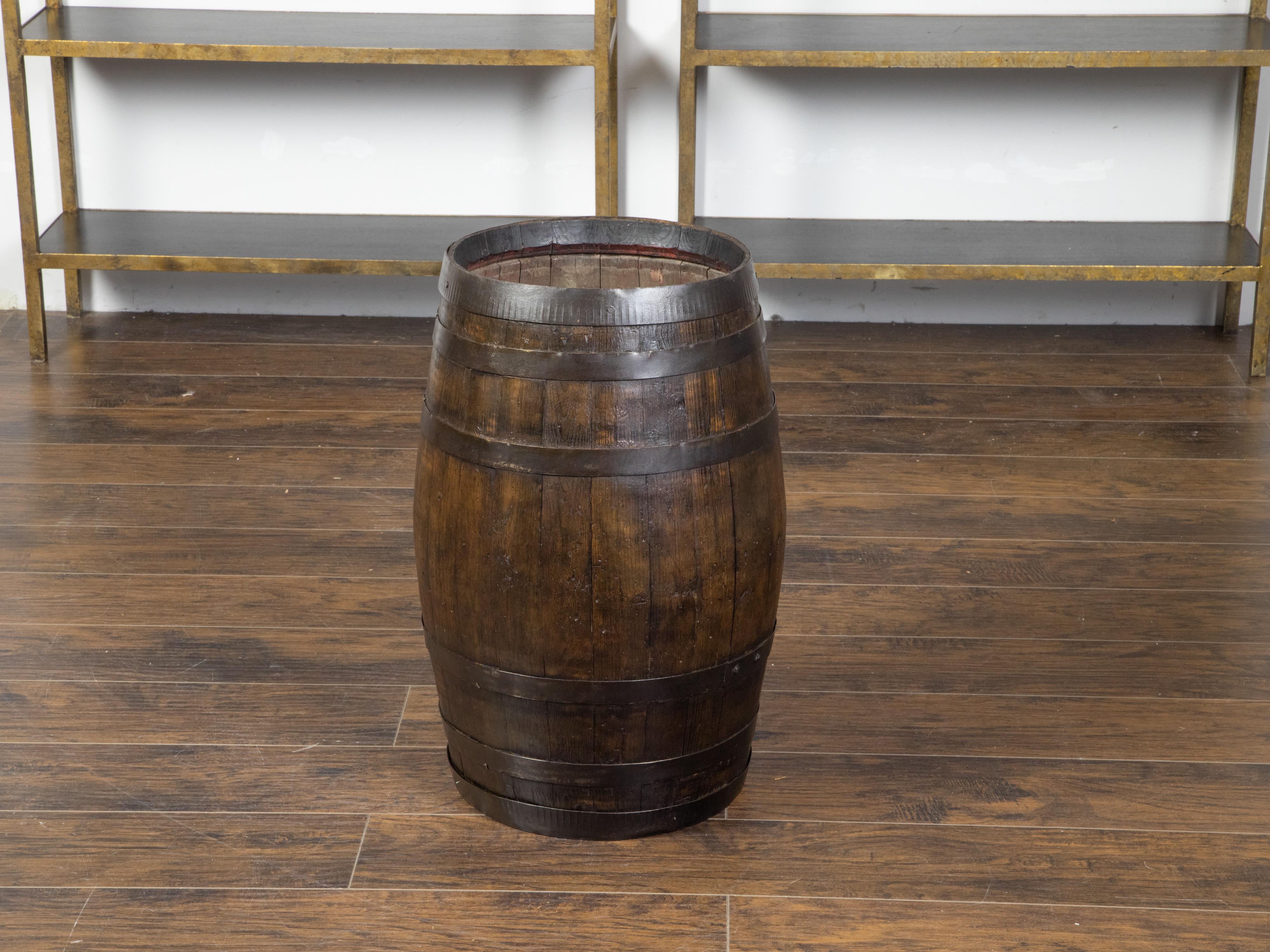 An English rustic oak barrel from the late 19th century, with iron braces. Created in England during the last decade of the 19th century, this barrel features a sturdy oak body made of vertical slats strengthened by the horizontal iron braces that