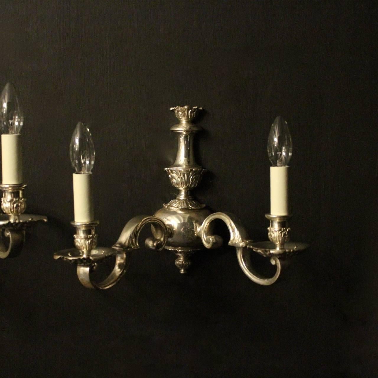 An English pair of silver gilded cast brass twin arm antique wall lights, the leaf scrolling arms with circular leaf bobeches drip pans and bulbous candle sconces, issuing from a decoratively cast elongated tapering backplate, nice original silver