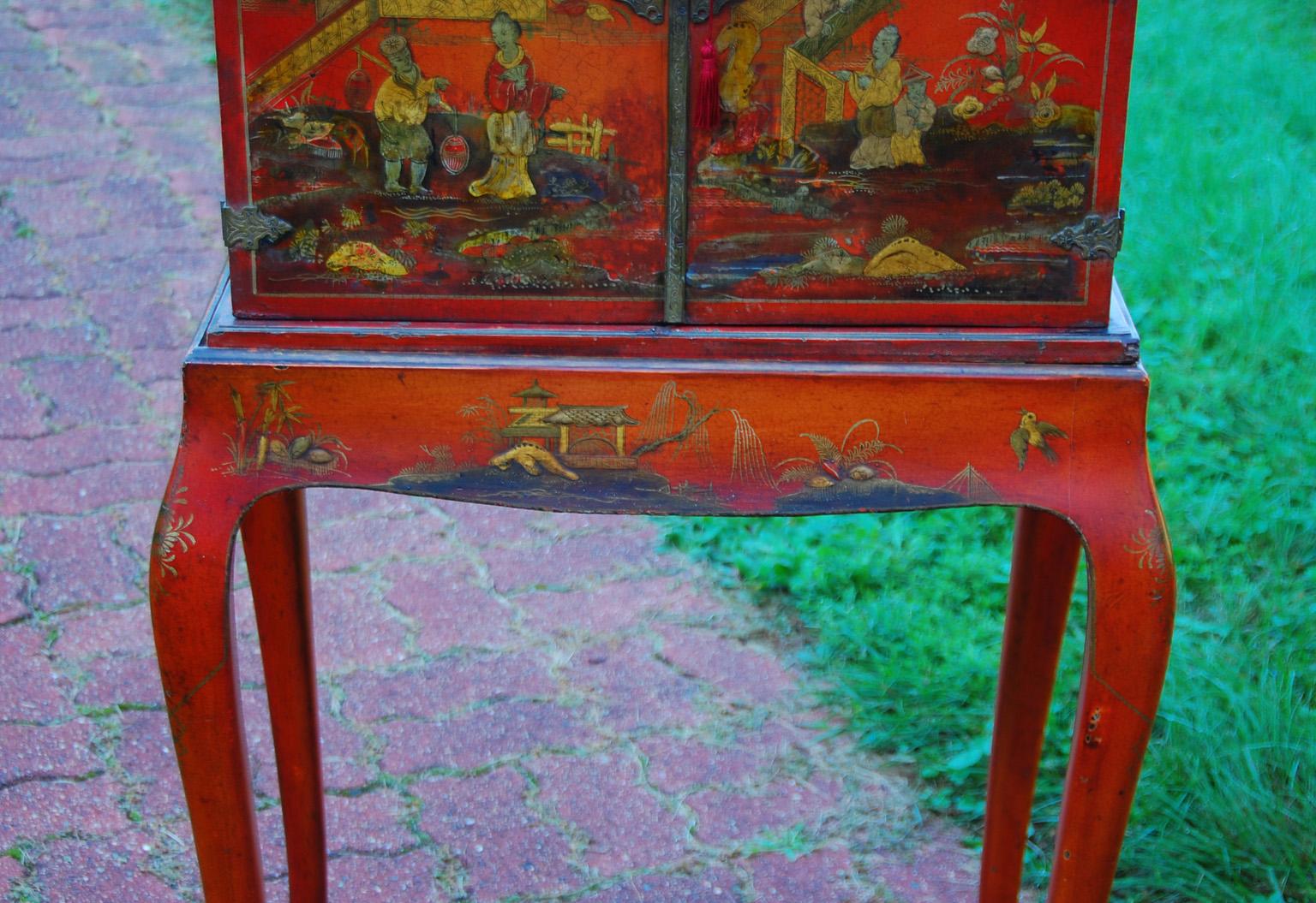 English late 19th century red chinoiserie lacquered cabinet on original cabriole leg stand. The two cabinet doors open to reveal eight black chinoiserie decorated drawers. This diminutive cabinet retains all of its original brass engraved fittings