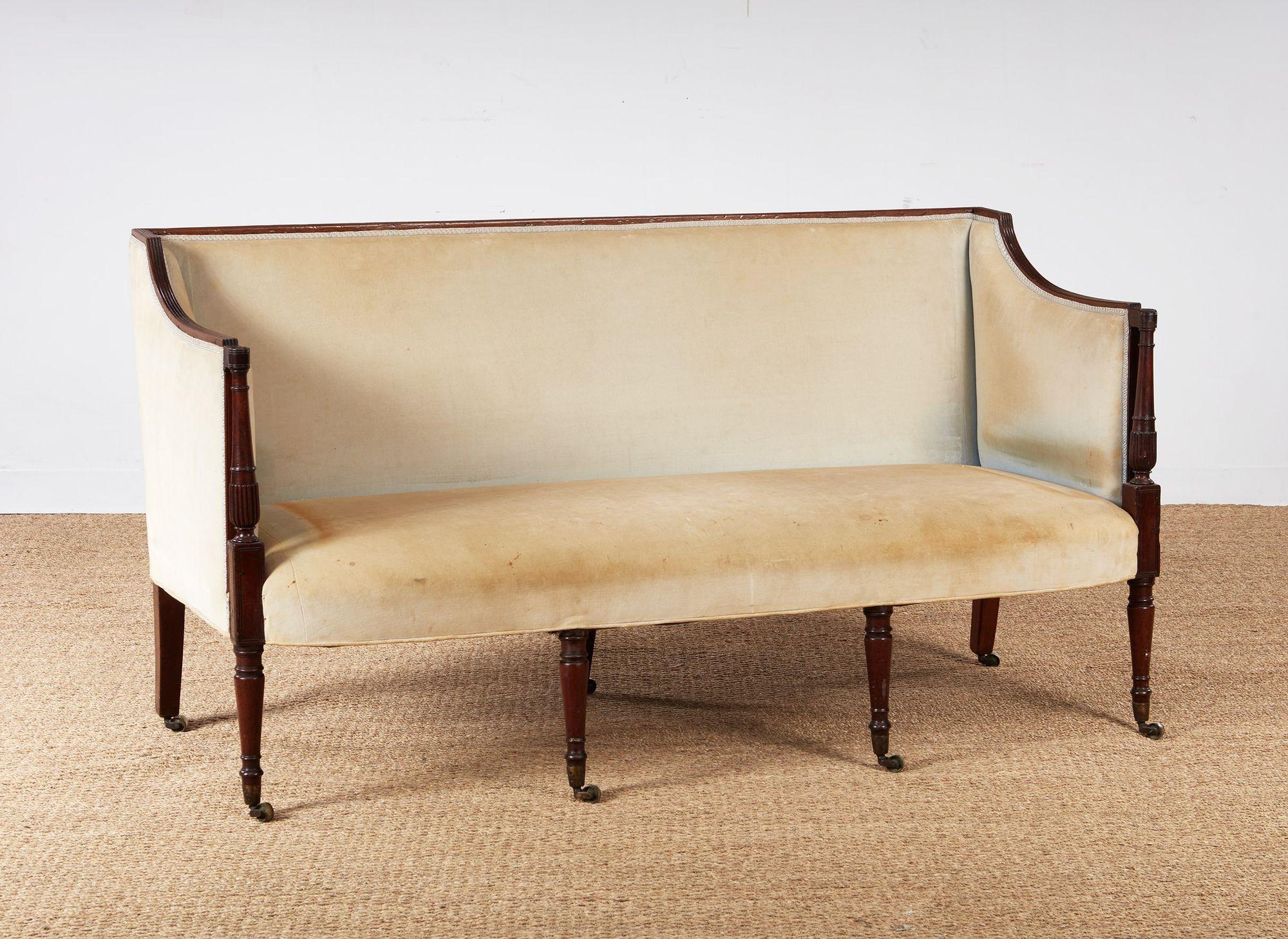 A late Georgian settee having upholstery to front and back with mahogany frame featuring reeded top edge, balustrade turned column arm supports and four tapered ring turned legs to front with three sabred legs to back.  A stylish and tailored
