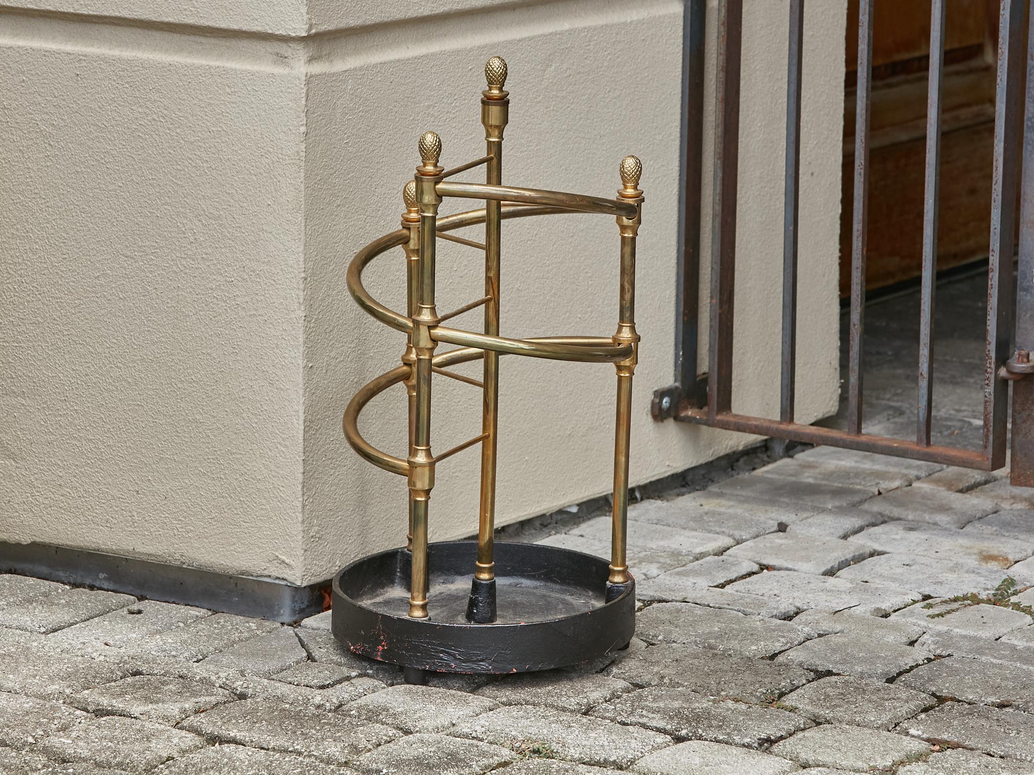 An English Late Victorian era brass umbrella stand from circa 1900 with pinecone motifs and iron base. Embrace the timeless elegance of the Late Victorian era with this exquisite English brass umbrella stand, circa 1900. Its captivating pinecone