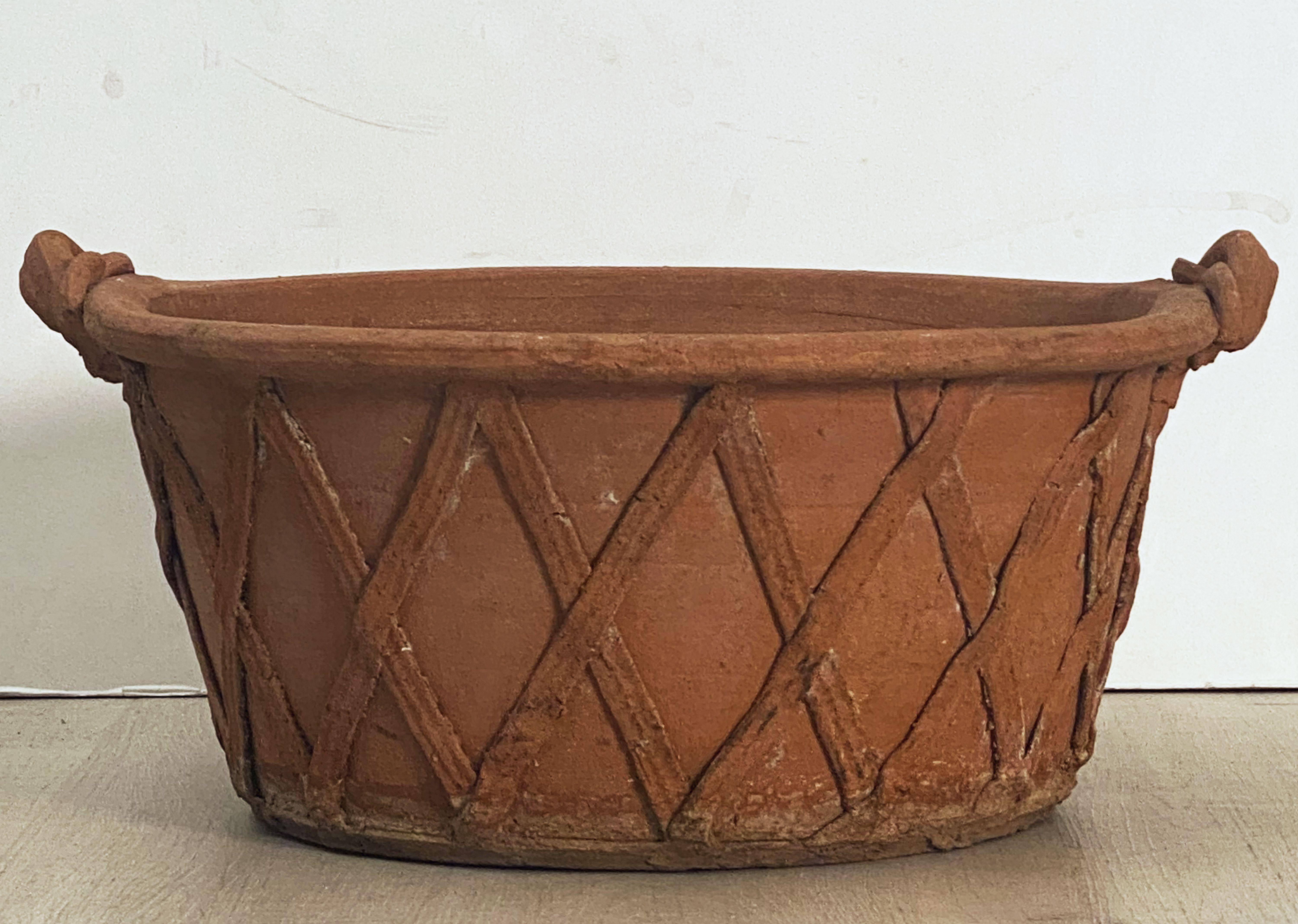 A fine large English round garden urn or planter pot or bowl of terracotta, 20 1/2 inches in diameter, featuring a stylized lattice or strapwork raised relief around the circumference and a rolled edge to the rim and handles.

Dimensions: Height 9