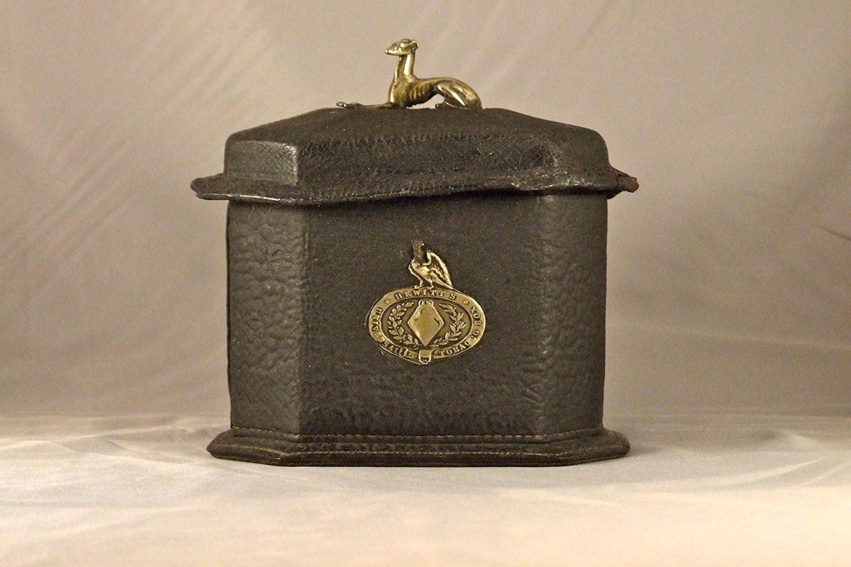 An English 19th century tobacco caddy of tin covered in stitched shagreen, of oblong hexagonal form with a lid surmounted by a silver whippet, retaining remnants of label 