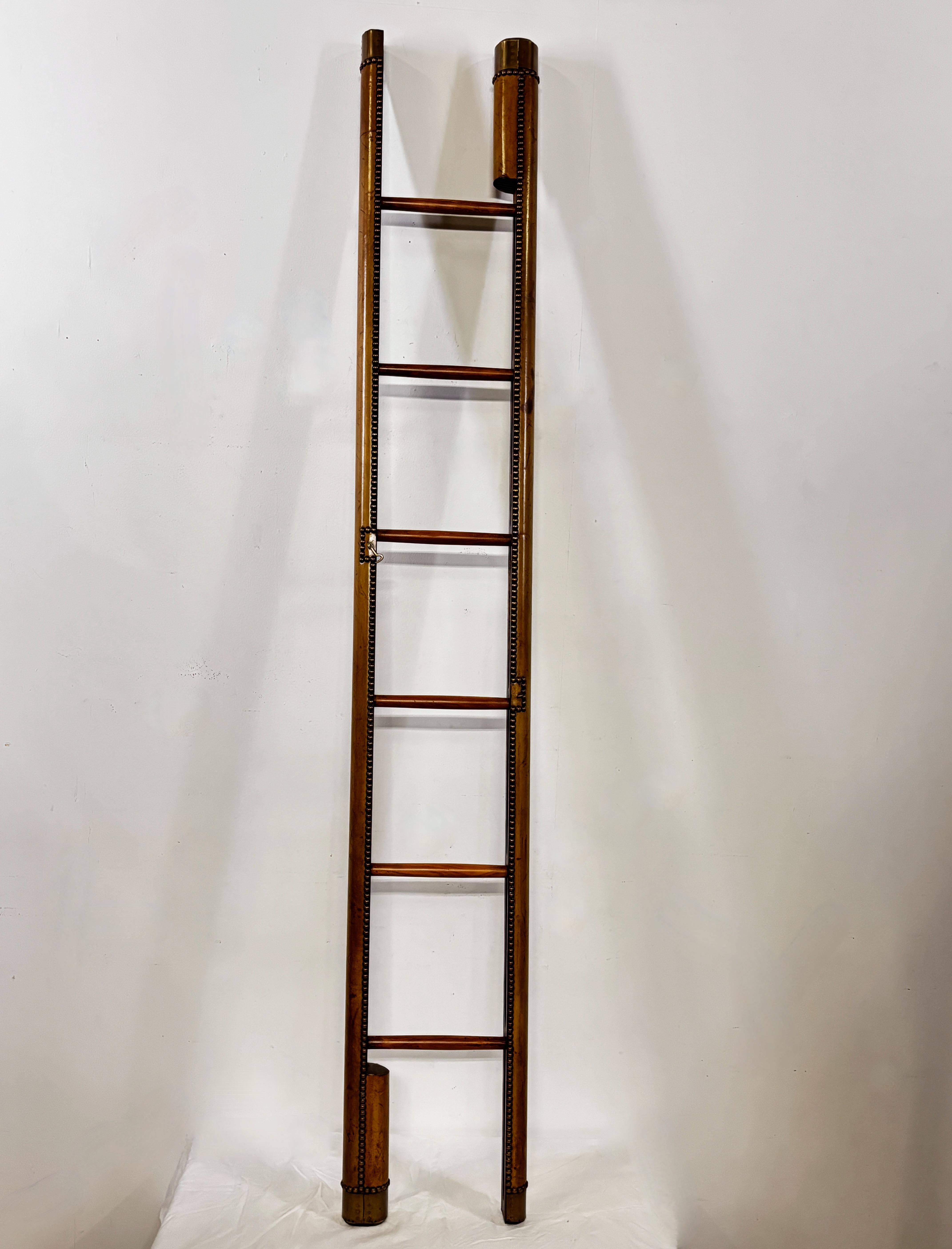 A Georgian style library elephant ladder, in walnut and wrapped with a brown leather which is accented by nailhead trim. The ladder folds into a pole with a mechanism and has a brass cap on both ends. A brass hook and latch is affixed to the ladder