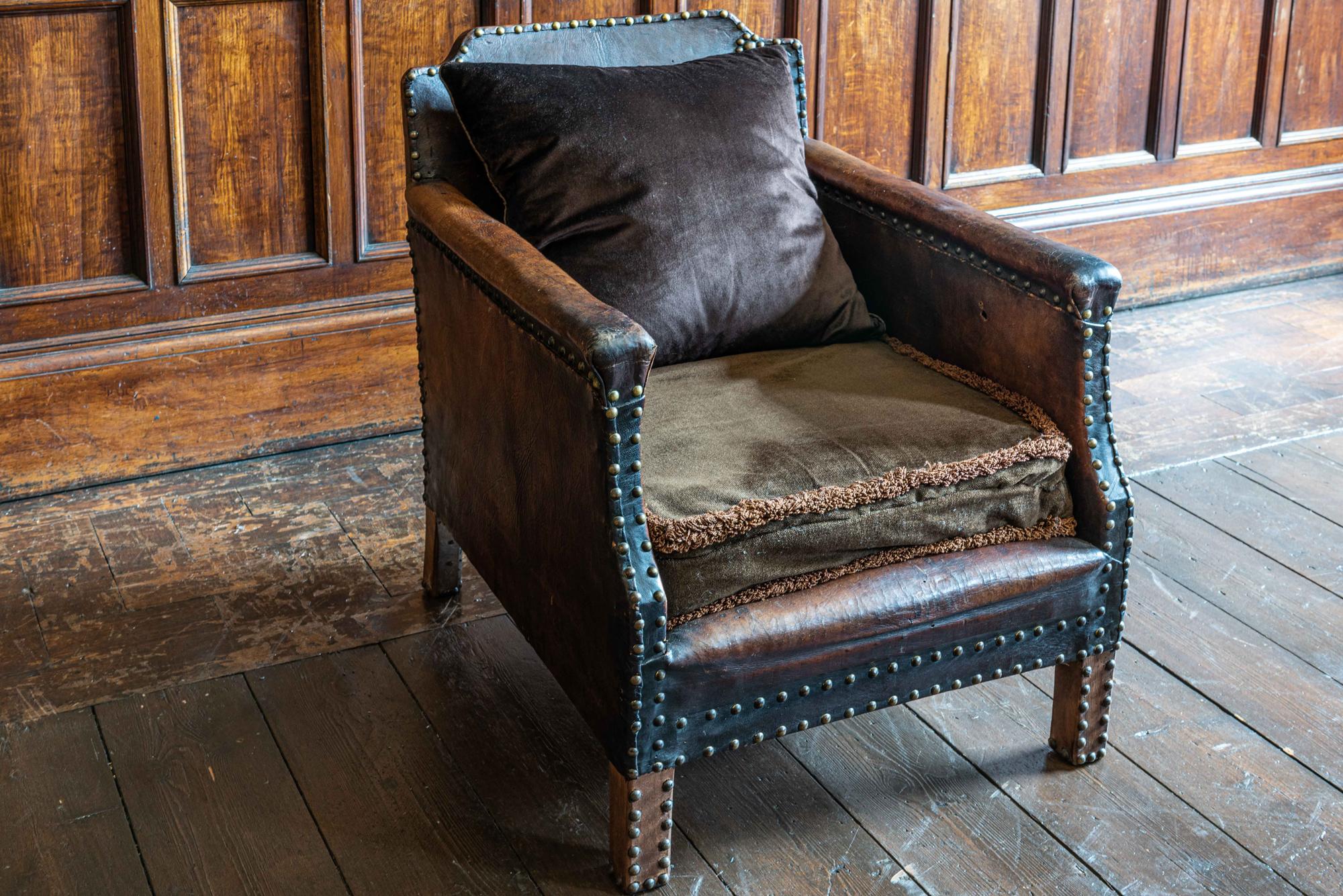 English leather and brass studded armchair
circa 1920.

Excellent colour, shape and worn patina, sprung base with velvet seat pad and feather filled velvet cushion.
Small hole on the inside arm.

Measures: 60 W x 80 D x 71 H (seat height 37cm).