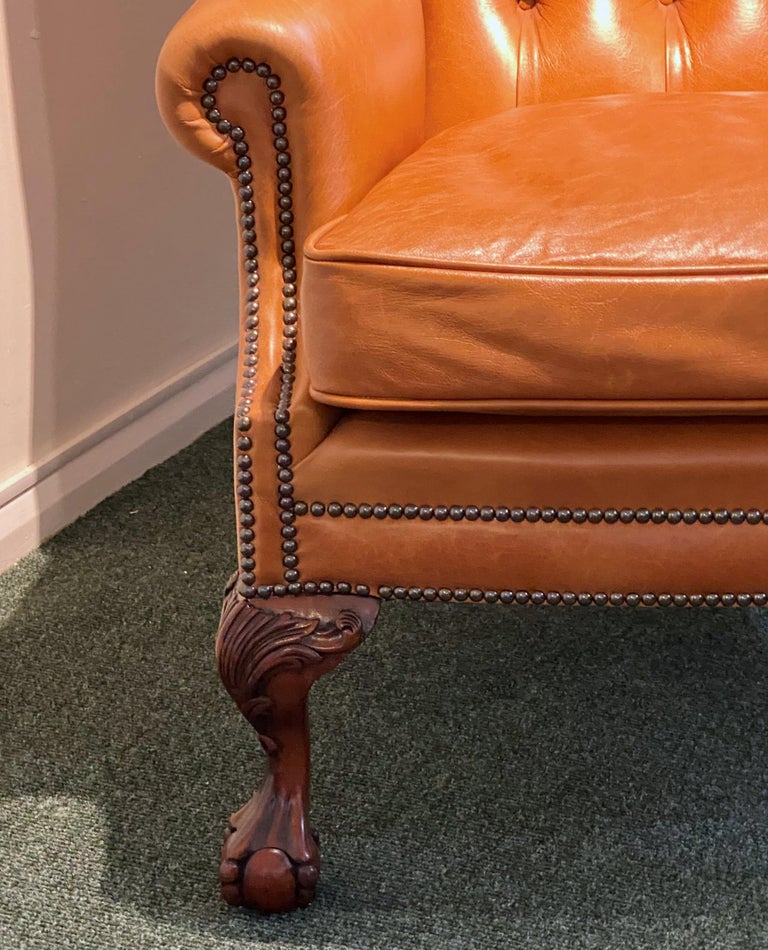 This classically 18th century styled English leather wing armchair features rolled back arms and metal stud detailing. The chair is upholstered in beautiful burnt sienna soft leather with a separate feather filled seat cushion, and a deep buttoned
