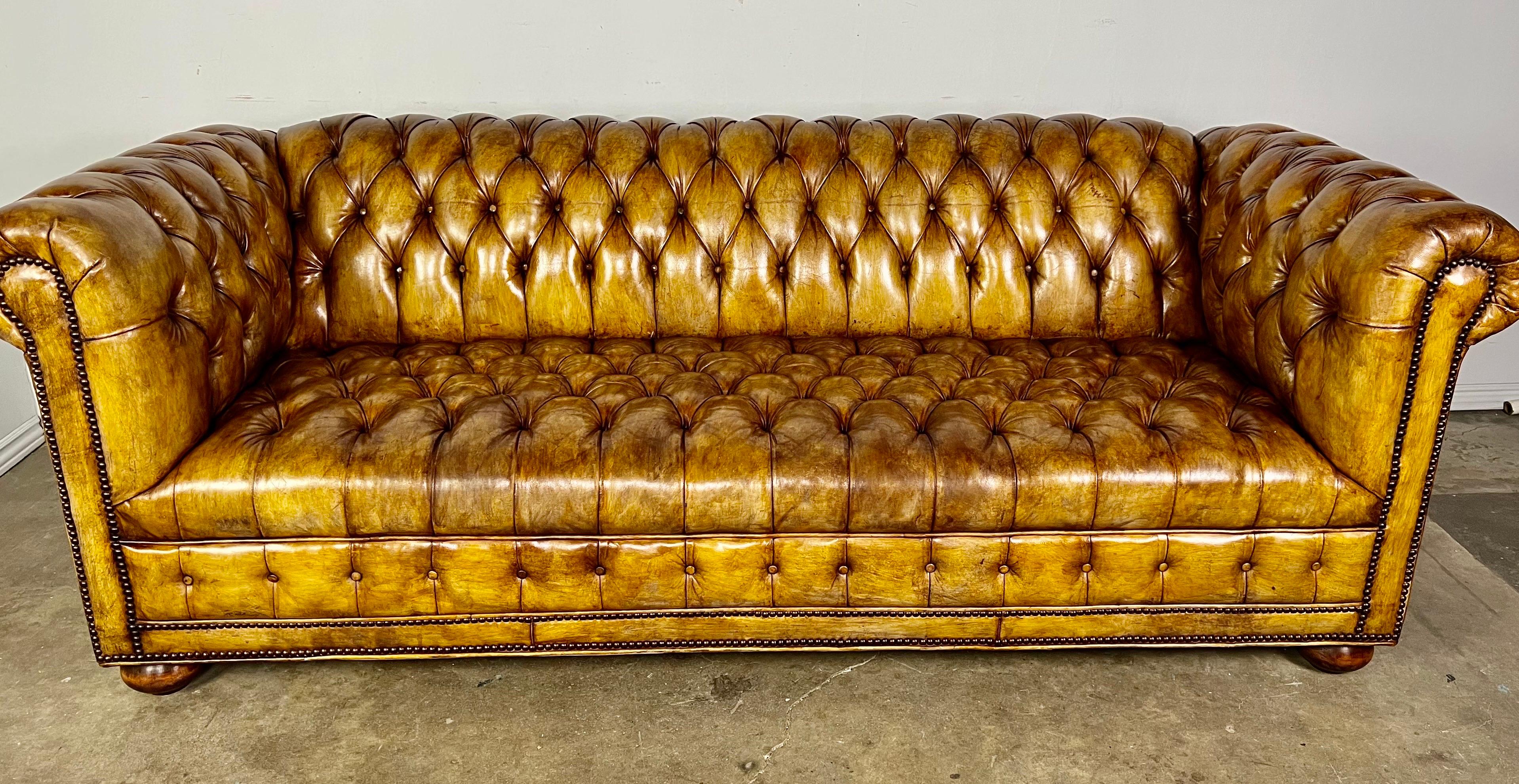 Early 20th century English leather tufted Chesterfield sofa with nailhead trim detail. The sofa stands on four traditional bun feet. The sofa is upholstered in a tobacco colored leather and has developed a beautiful patina over the years. Excellent
