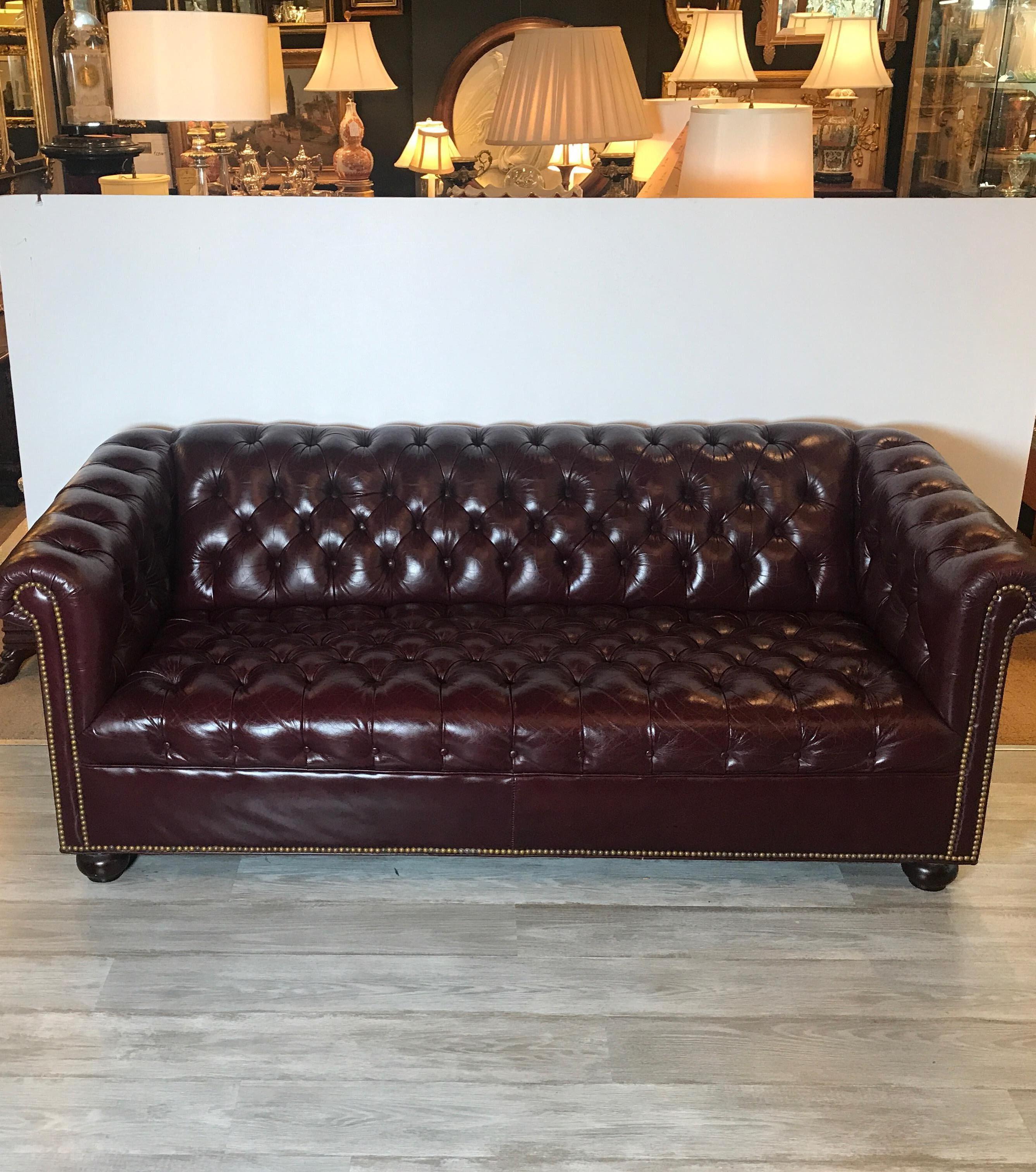 A well cared for English cordovan leather Chesterfield sofa with antiqued nailhead trim. The tufted attached seat back and arms with brass nailhead trim along the arms and bottom. The sofa is a perfect size at 76 inches long with original well cared