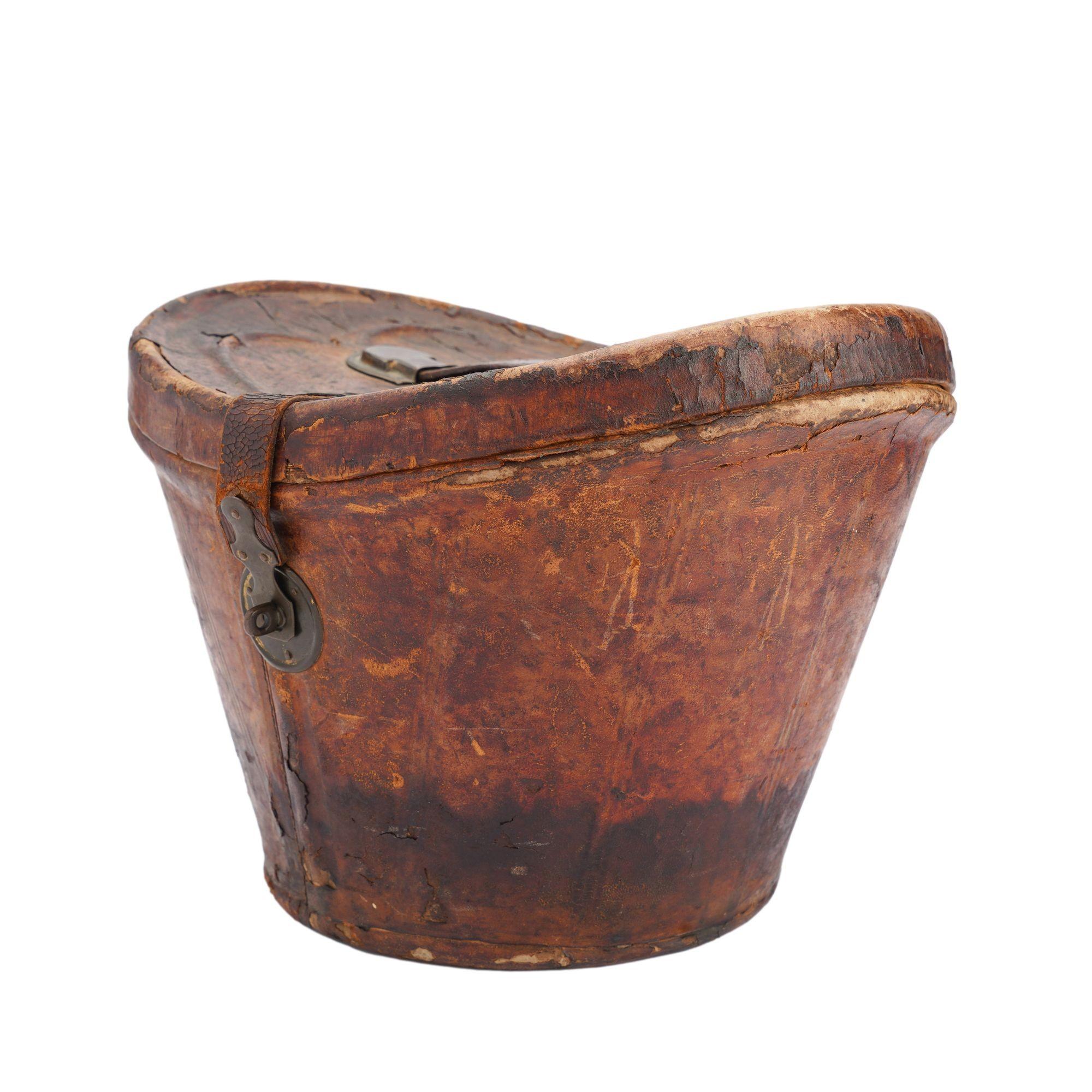Distressed leather hat box for a man’s wide brim top hat. The lid is hinged and has a metal closure. The handle and strap stays are molded metal. The interior retains its original cream and green patterned paper lining.
England, circa