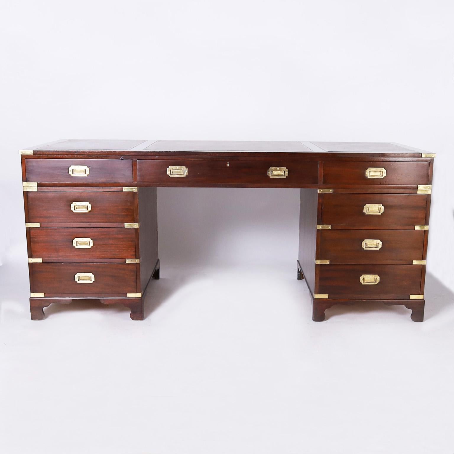 Impressive antique English campaign desk crafted in mahogany in a faux partners form featuring a generous scale with a wide kneehole, three tooled brown leather panels on top, nine drawers in the front, brass campaign hardware, pullout leather