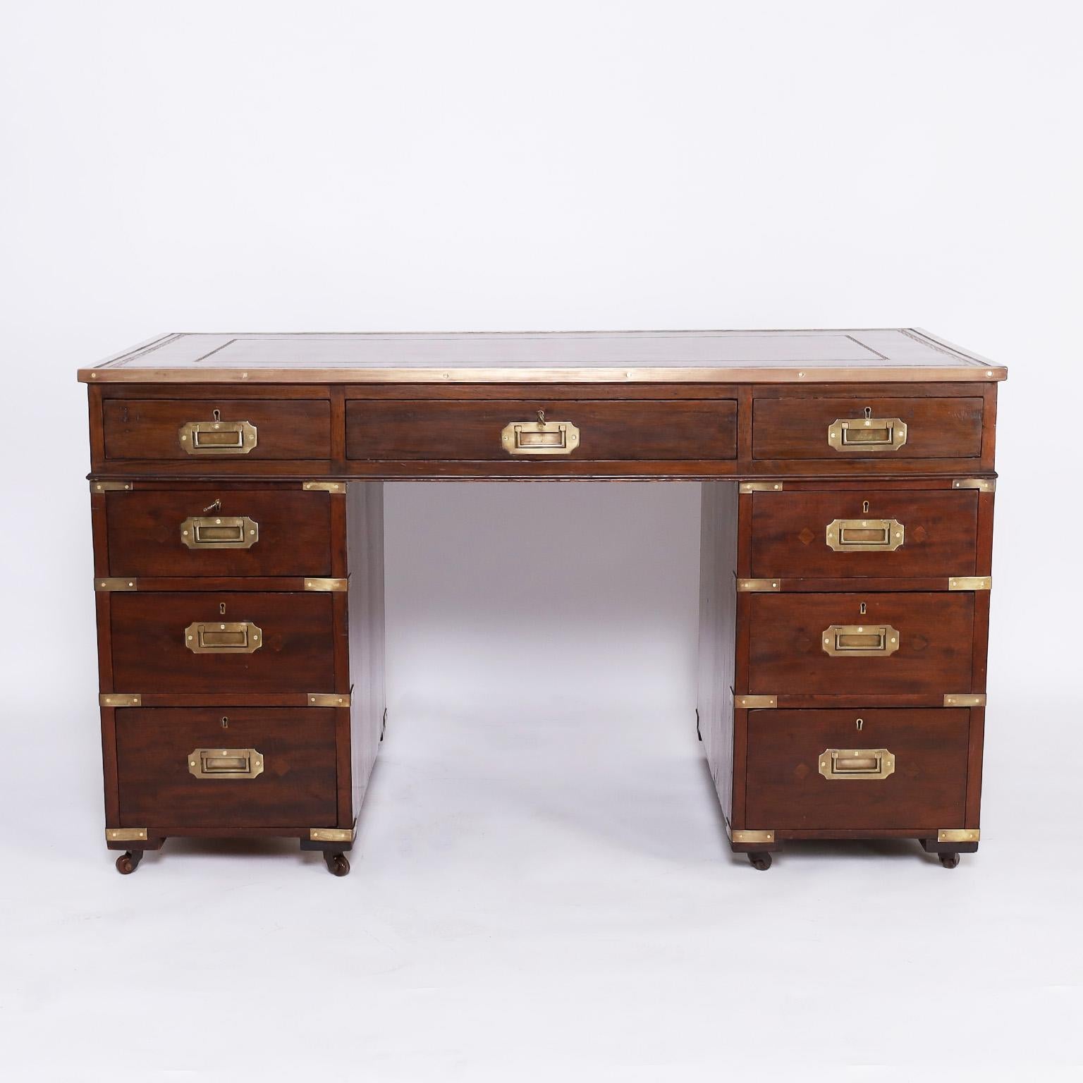 Handsome 19th century British colonial campaign desk with a brown tooled leather top, brass hardware, keys to the top and side drawers, and sits on porcelain casters.