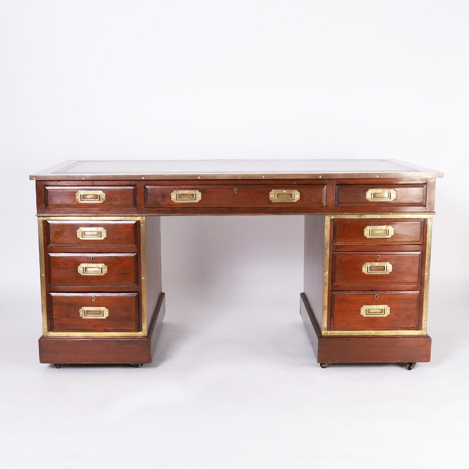Impressive 19th century British colonial campaign desk crafted in mahogany and featuring a tooled brown leather top, brass campaign hardware, beveled drawer fronts, and block feet elevated by inset casters.