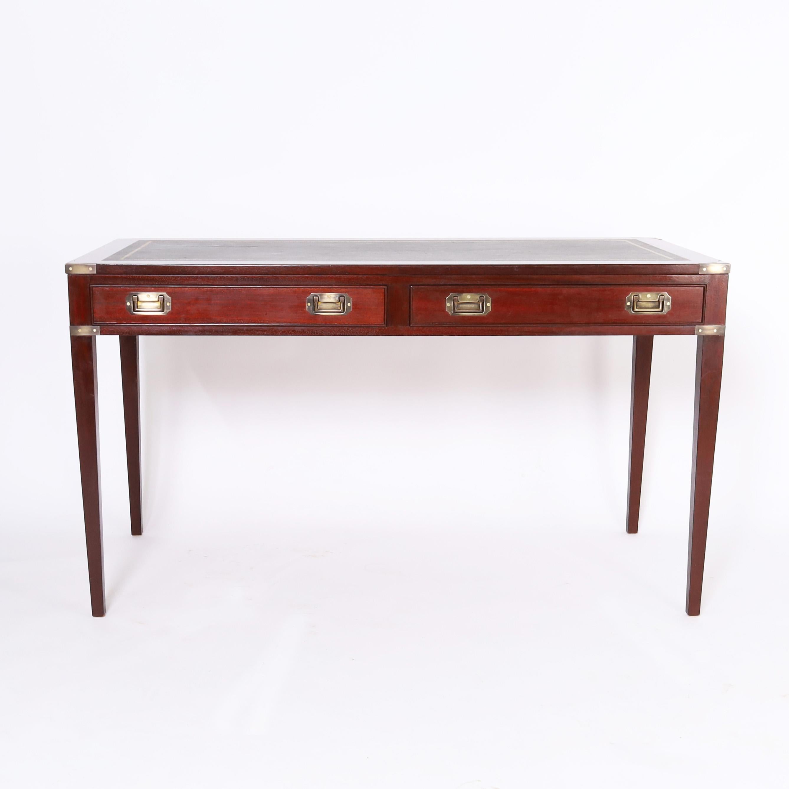 Handsome English Campaign style writing desk crafted in mahogany with a tooled green leather top, brass hardware, two drawers in the case, and elegant tapered legs. 