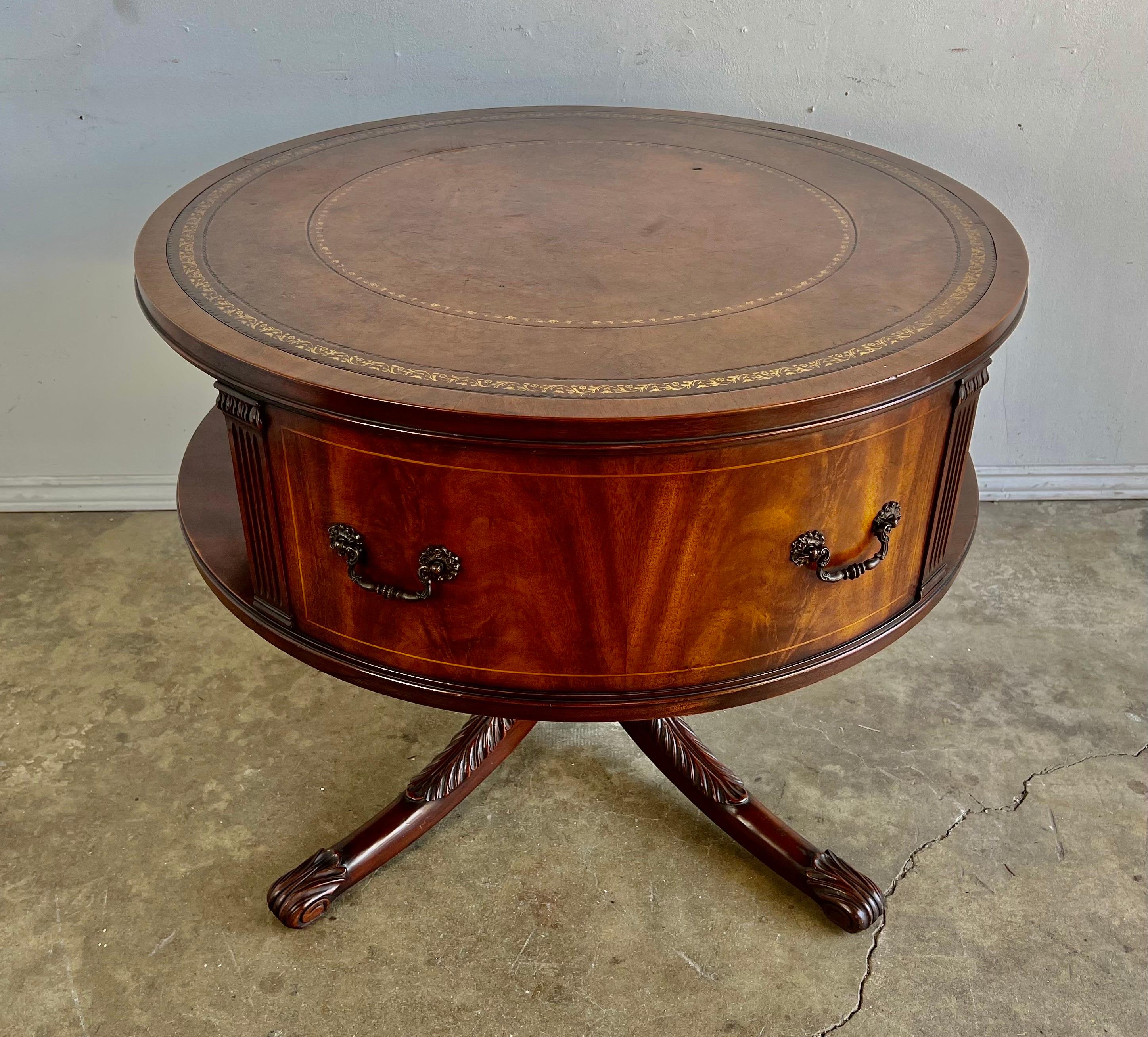 English leather top Drum table that stands on a four curved legs with carved acanthus leaf detail. The brown leather on the top is beautifully gold embossed around the edge of the top. The table is constructed with flame mahogany. The inside of the