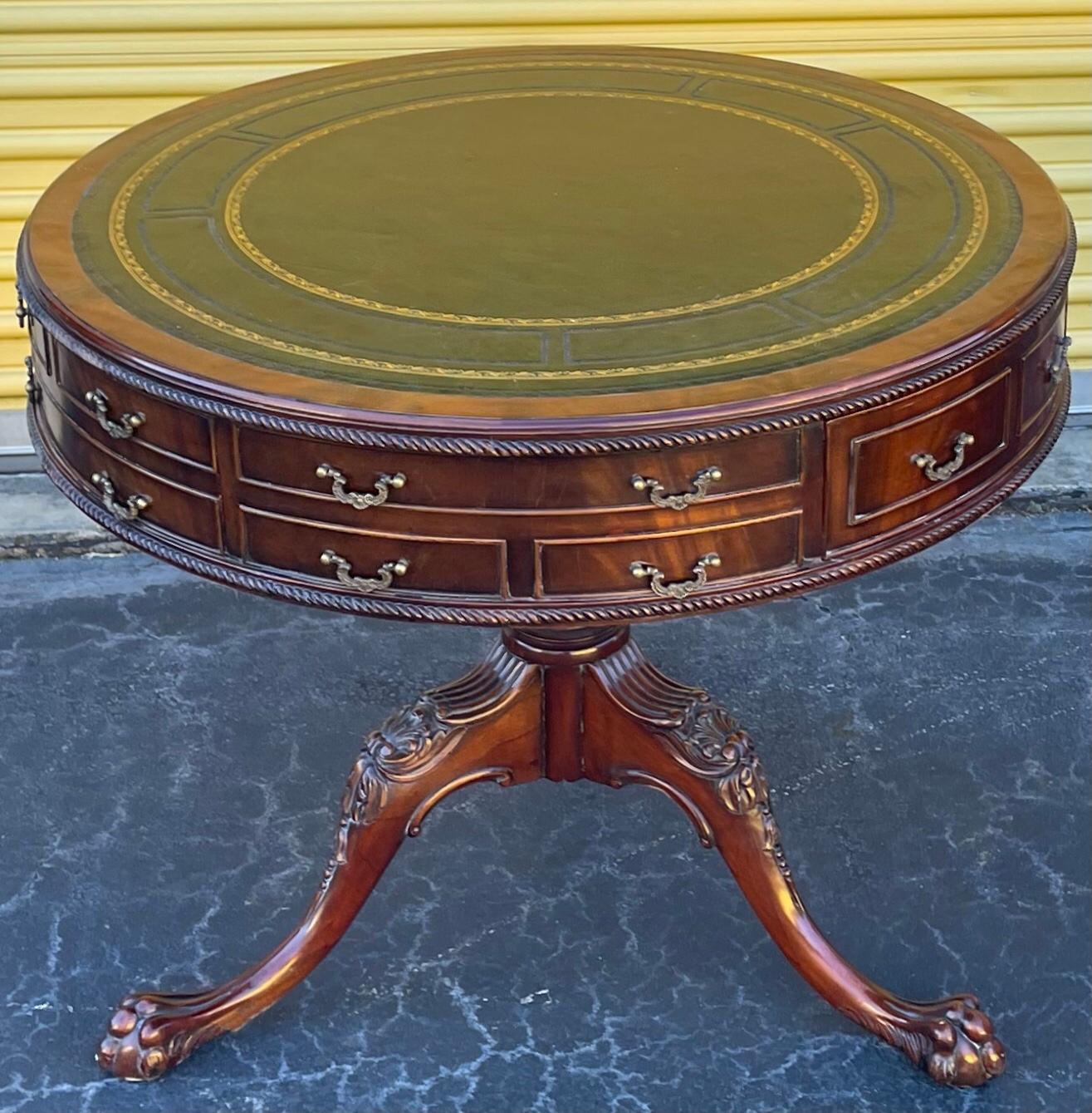 This is a lovely English drum table with Georgian styling. It has a green leather top. The frame is carved mahogany with brass hardware. The drawers have dovetail construction. It is a reproduction of a period piece and is unmarked.