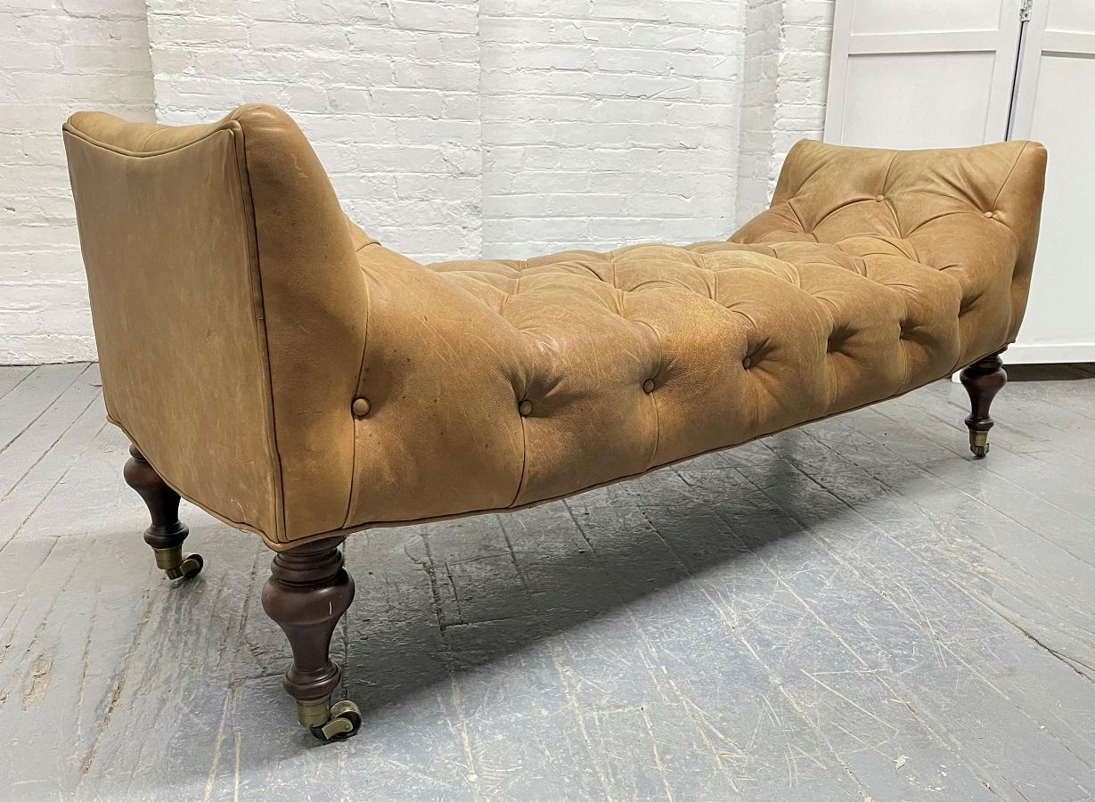 English leather tufted bench with solid wood legs and brass casters.