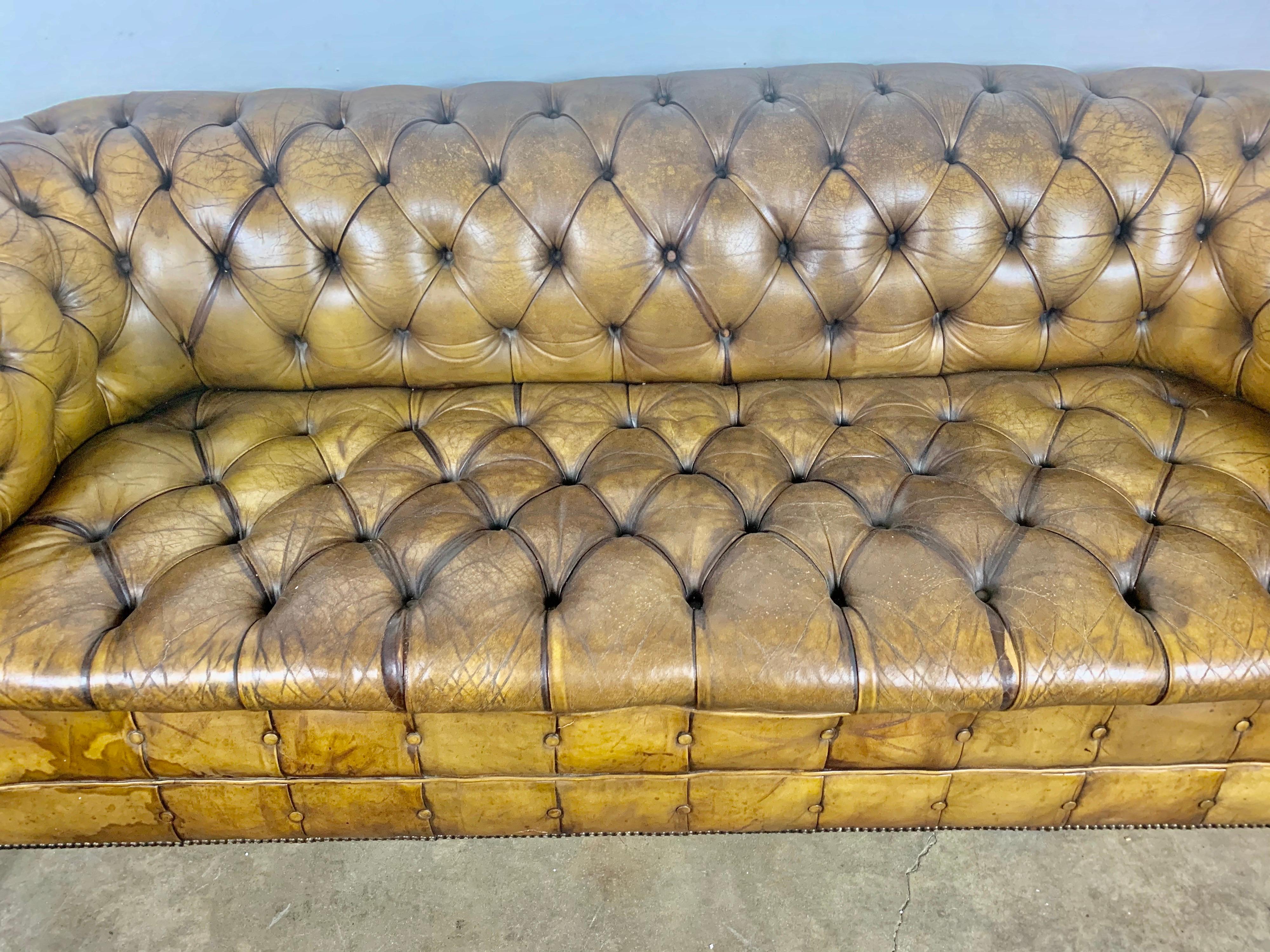 Handsome English leather tufted Chesterfield style sofa with lion paw feet and nailhead trim detail. The leather is beautiful worn with distressing throughout showing the history it has had along the way. Light tobacco color.