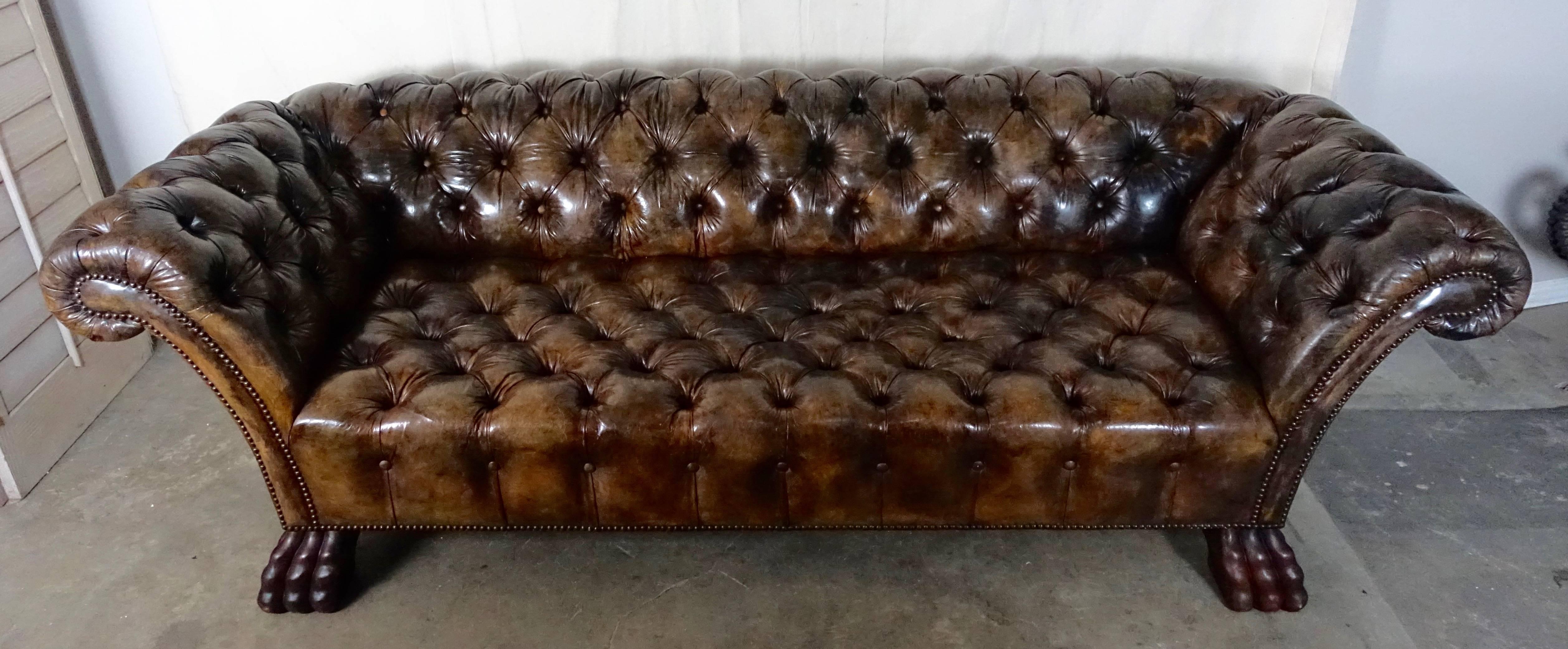 Handsome early 1940s leather tufted sofa standing on four hand carved paw feet. Measures: 16” SH. Antique brass nailhead trim detail. The sofa has developed a rich patina and is in excellent condition.