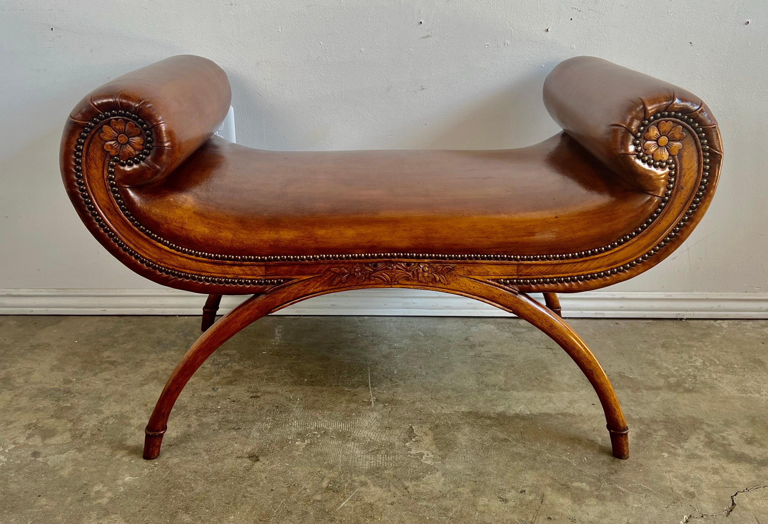 English Regency style walnut carved bench upholstered in a tobacco colored leather with nailhead trim detail. The bench has matching scrolls on both sides that give it beautiful lines. The simple arched legs are perfect with the scrolled arms of the