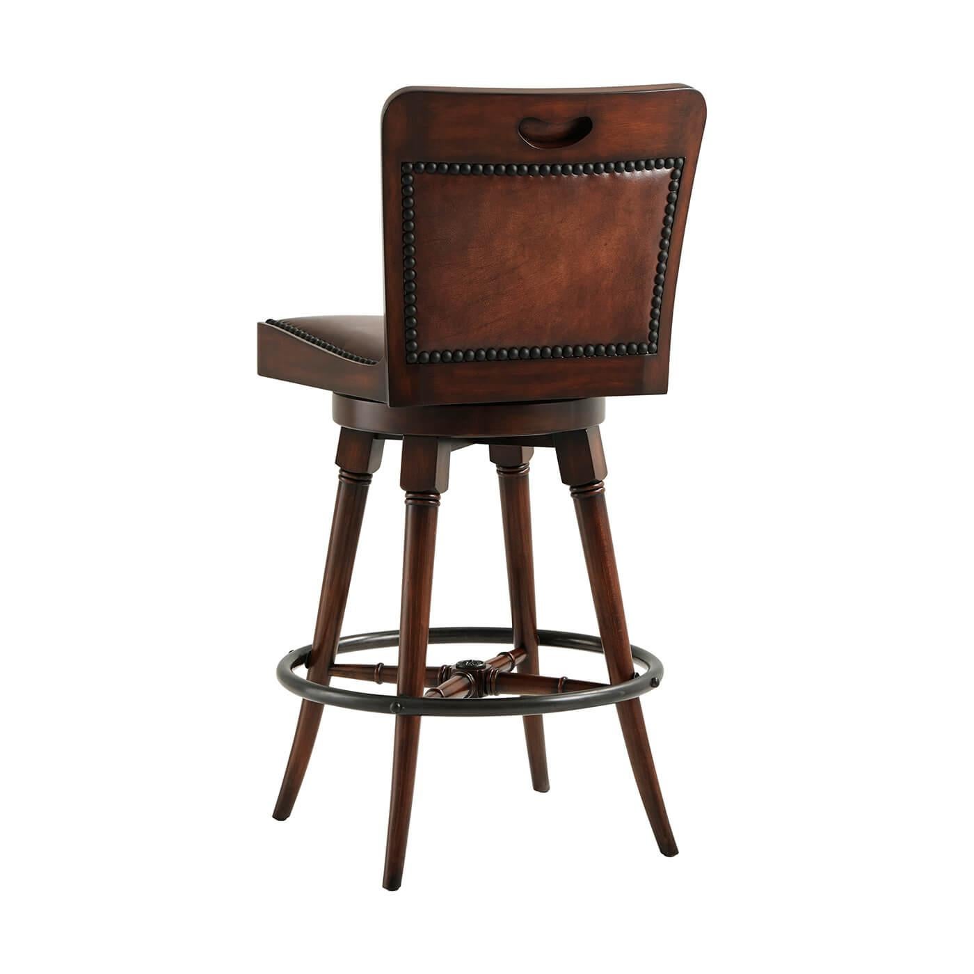 Tabouret de bar pivotant anglais en cuir. L'assise en bandoulière vieillie repose sur des pieds tournés à ébrasement, reliés par une entretoise en 