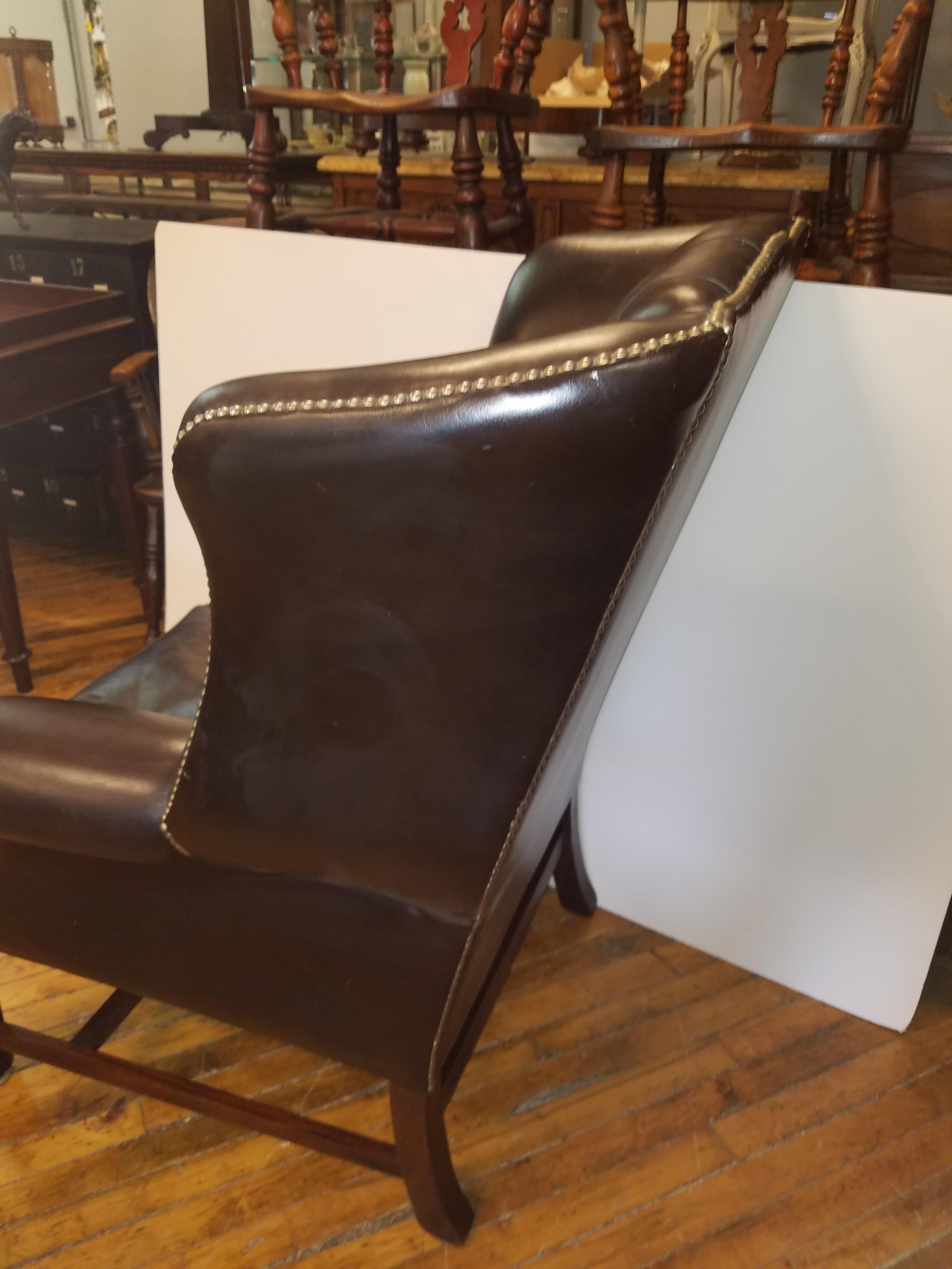 1950s English wingback chair in a dark brandy color leather with brass nailhead trim. The chair with shapely sides and deep tufted attached back and mahogany legs.

  