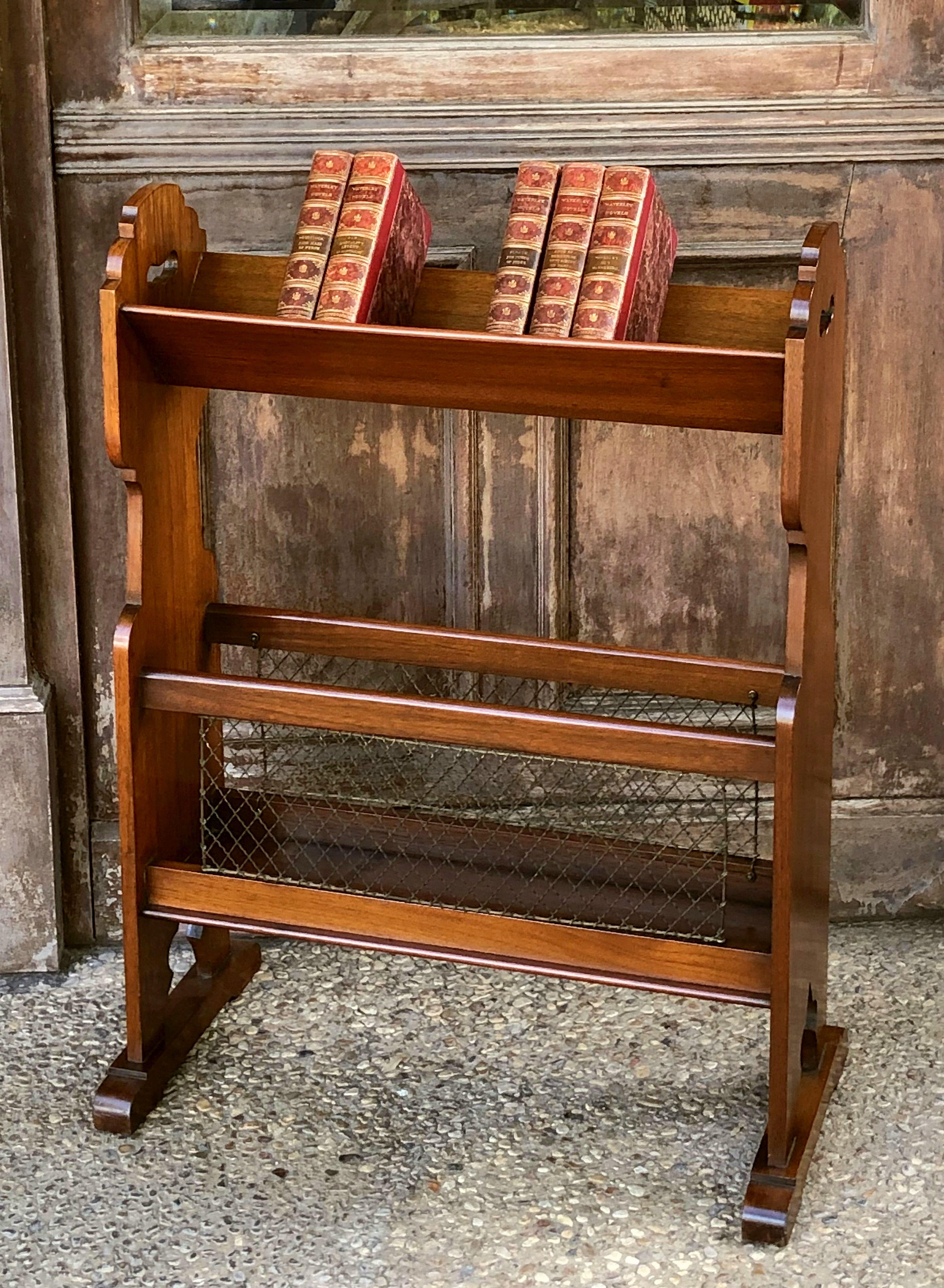 A handsome English two-tiered book trough or library book stand of walnut, from the Edwardian era, featuring a canted upper tier over a flat bottom tier enclosed by a brass grille, where magazines or other items can be stored.