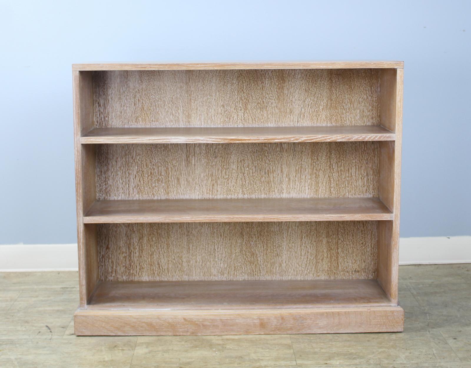 A simple and classic oak bookcase with it's original liming in the style of Heal's, a London maker of limed oak furniture. Handsome silhouette with a generous classic plinth at the base.  