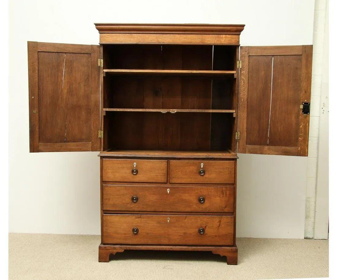 An early-to-mid 19th century English linen press in oak, in two parts, the upper cabinet with a pair of paneled doors, over a lower bank of 4 drawers with wood knobs and inlaid bone key escutcheons, all on ogee feet. 
Piece includes documentation