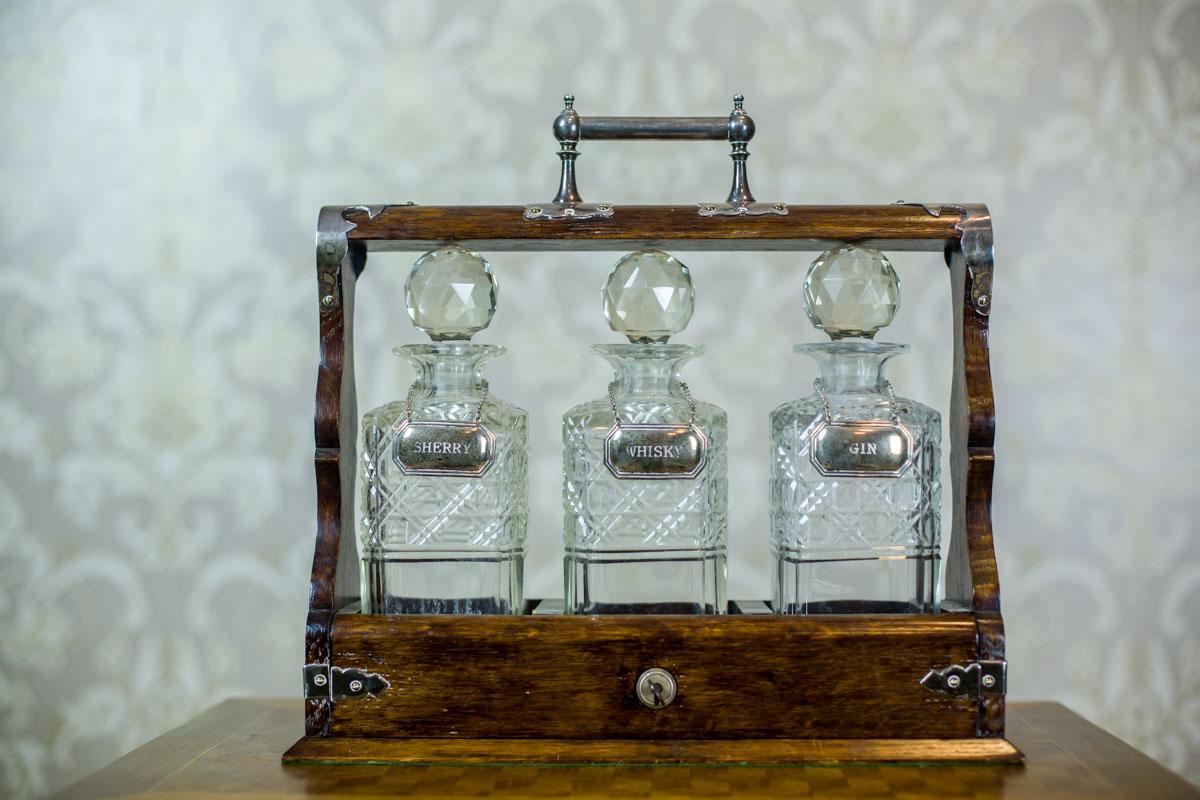 We present you three decanters: for gin, whiskey, and sherry.
They are hid in a wooden case that can be locked with a key; with a handle to move it around.
The whole is dated 1900.
The decanters are made of polished glass, with a capacity of 0.5