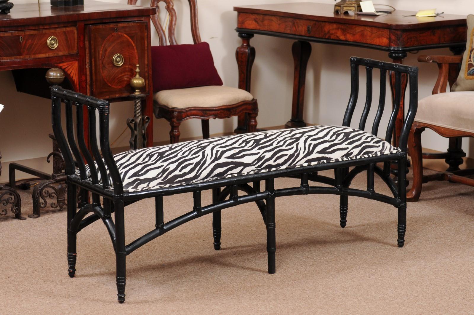 A 20th century English long black painted faux bamboo bench featuring arms, upholstered seat with zebra design and arched stretcher. 

  