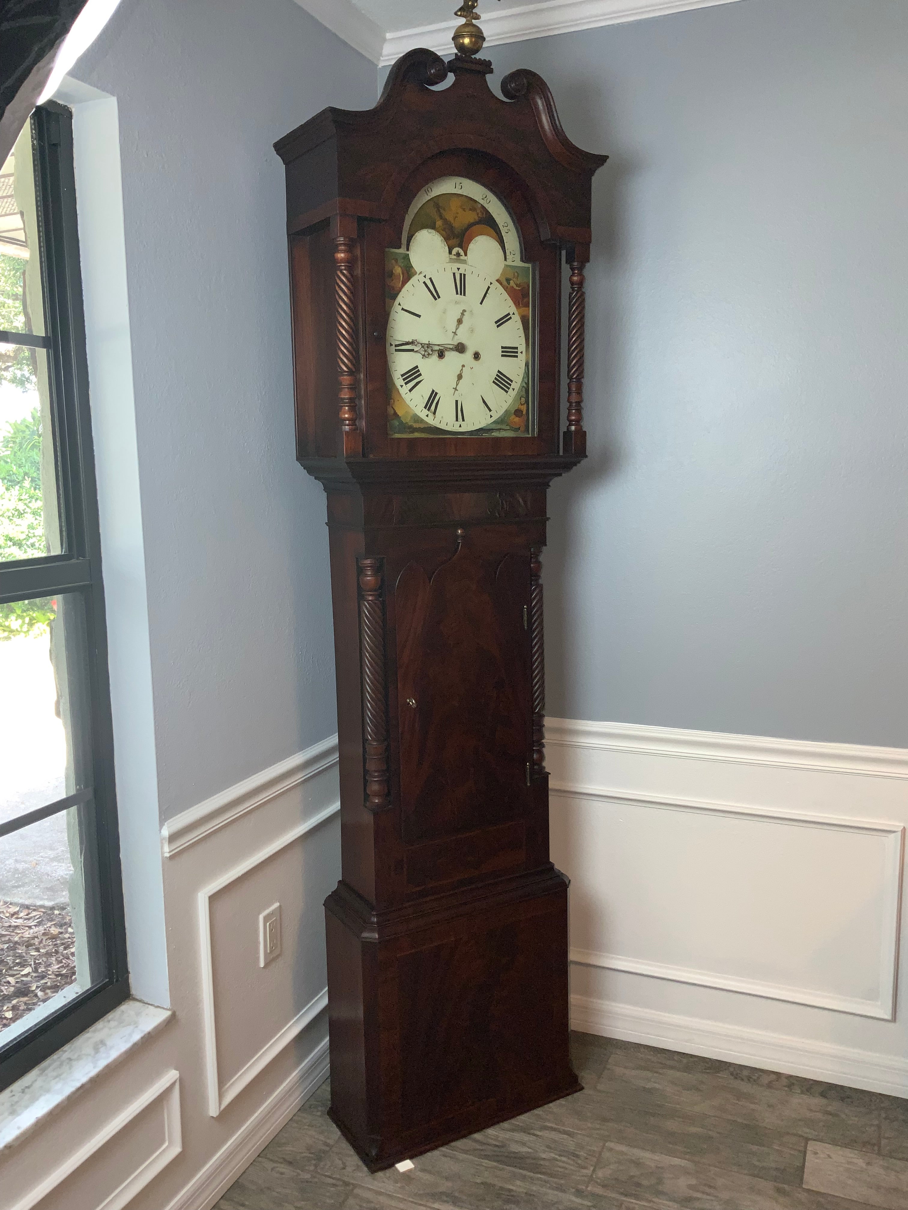 A very nice quality mid 19th century English Mahogany long case clock. Decorative figured Mahogany case with an arched hood with swan neck pediment. Polished pierced Brass hands.  Painted dial with phases of the moon and hemispheres.  False plate
