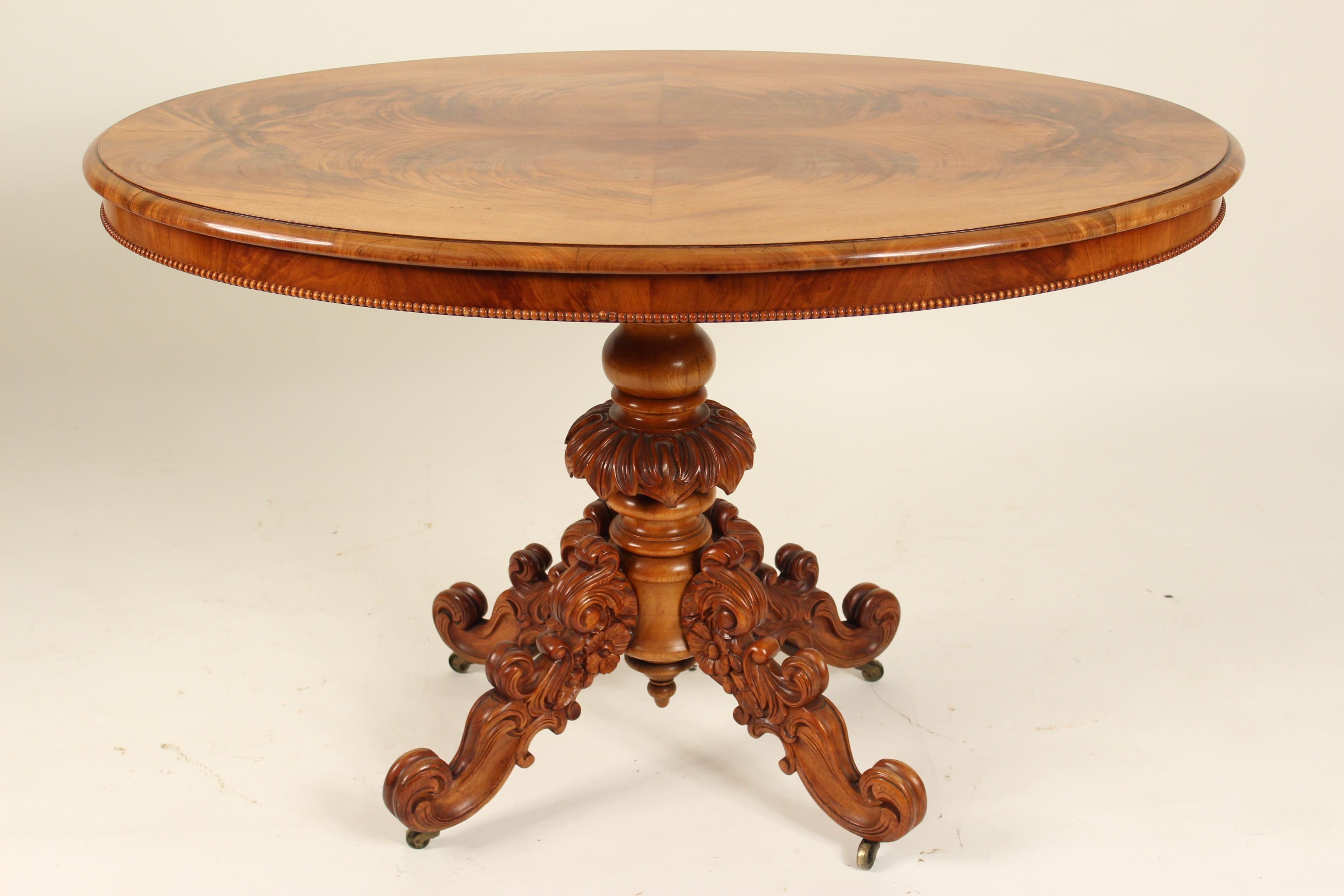 English loo table with an excellent book matched flame mahogany top and a vigorously carved pedestal base, circa 1900.
